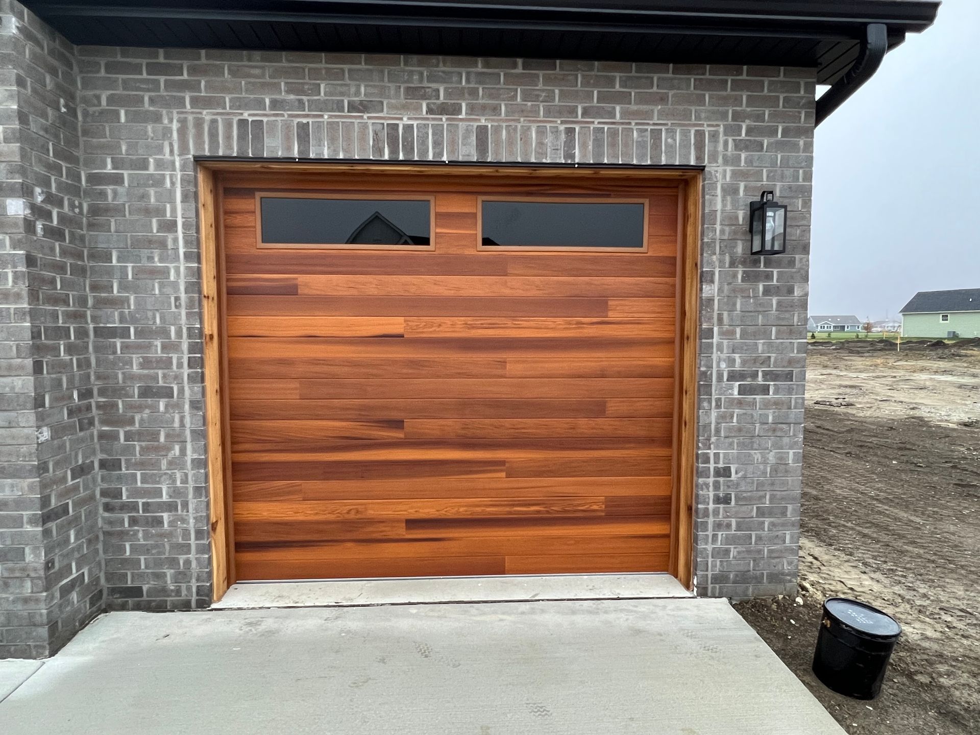 Wooden garage door with small windows on a brick house exterior, beside a concrete driveway.