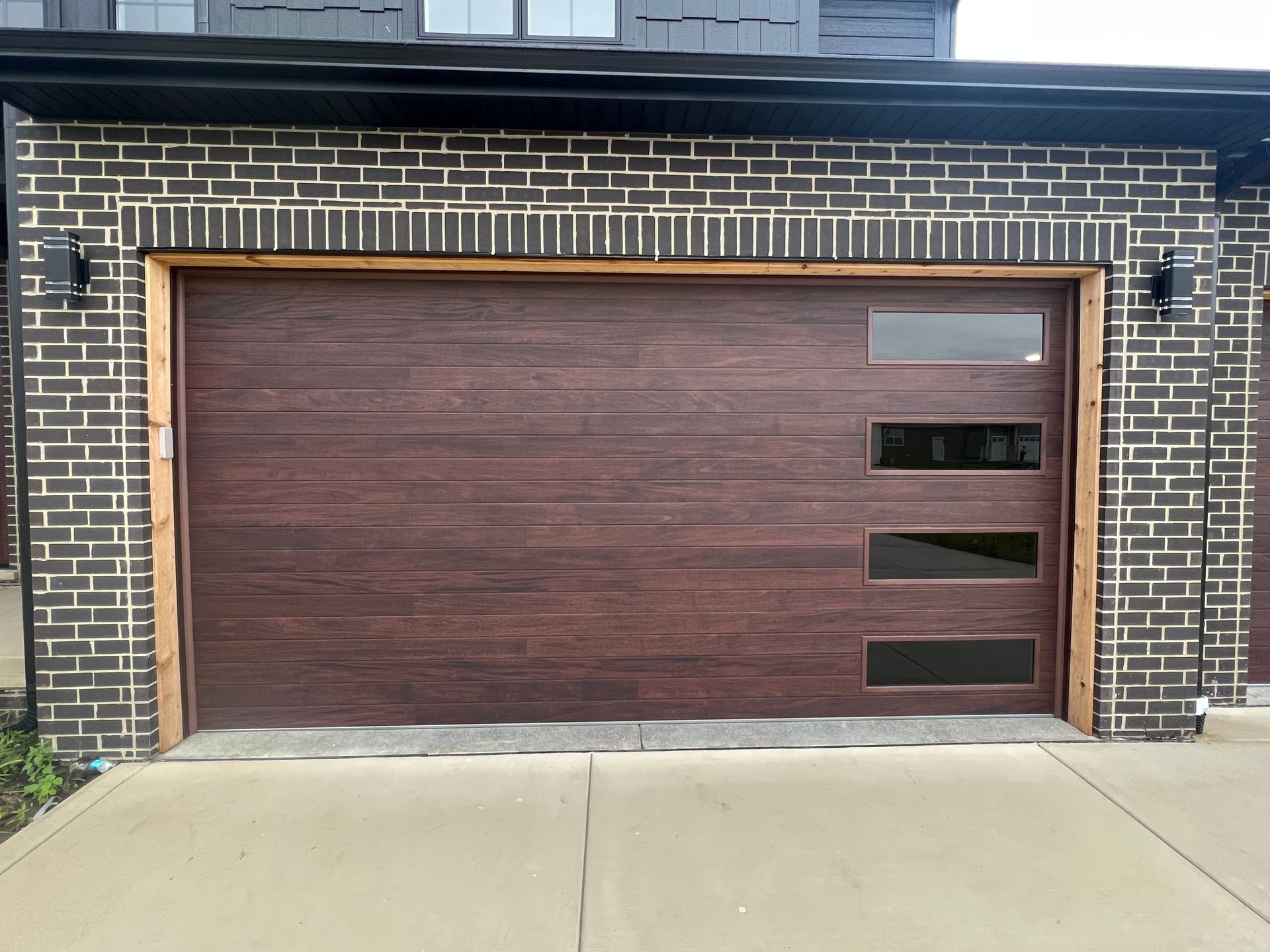 Modern brown wooden garage door set in a brick wall with concrete driveway in front
