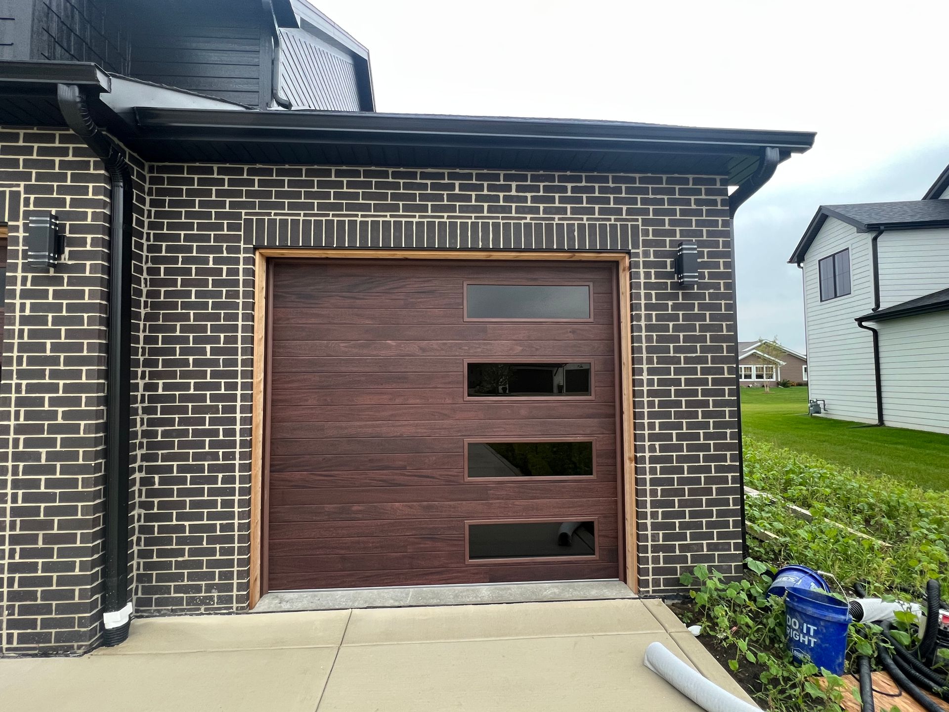 Brick house with a modern wood garage door and small side windows, beside a driveway and lawn