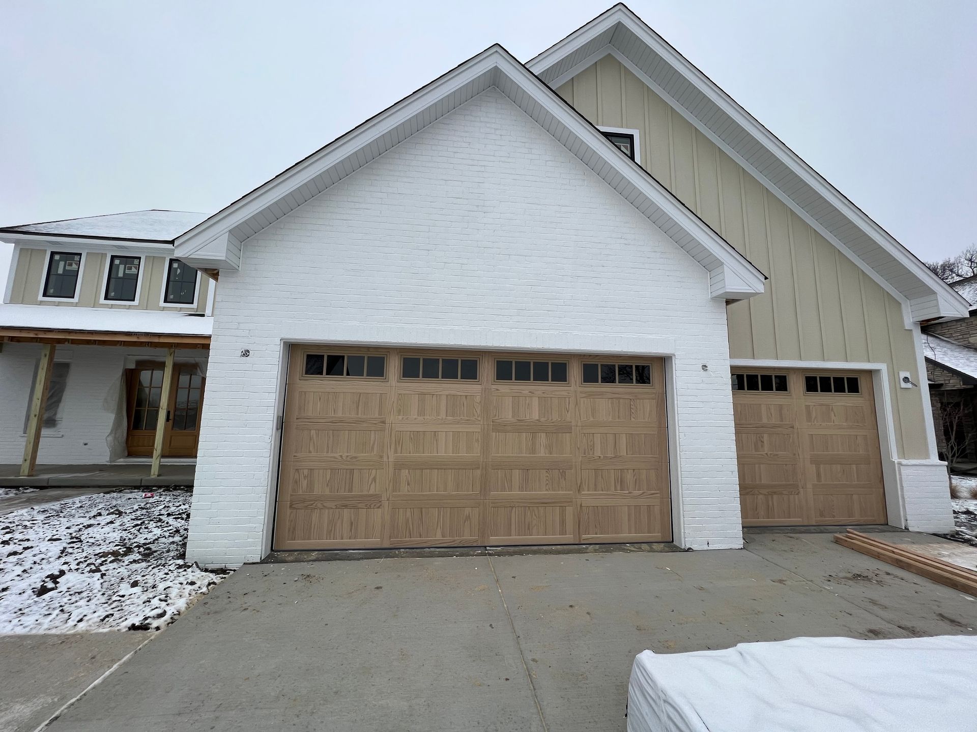 Snow-dusted suburban house with a white exterior and tan garage doors on a concrete driveway