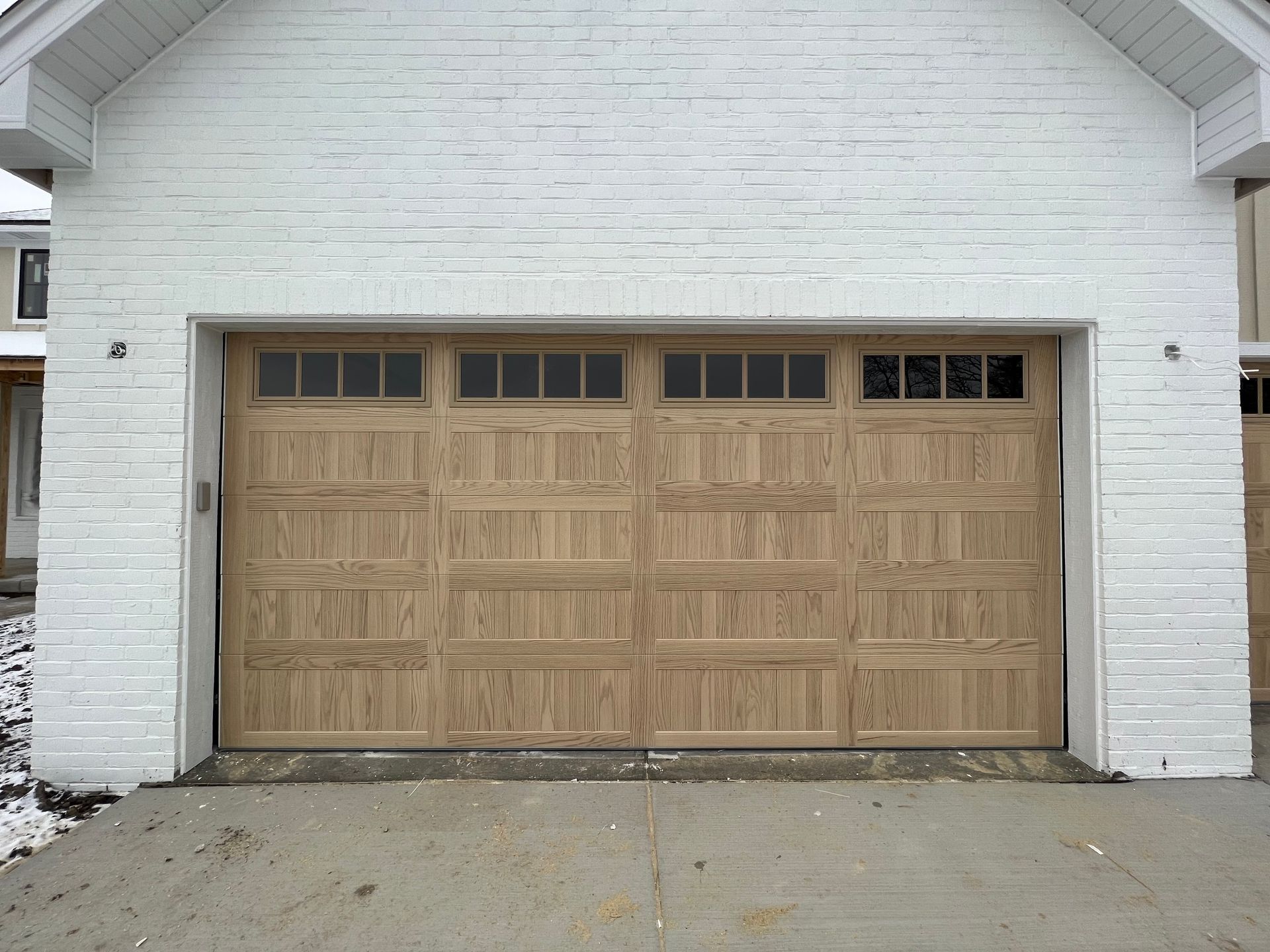 Tan garage door on a white brick house exterior with a concrete driveway