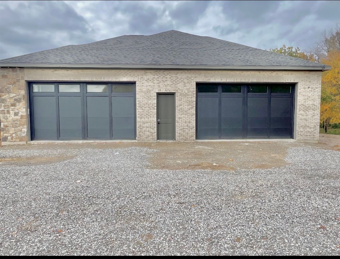 Modern stone building with large dark windows and a central door, fronted by a gravel lot.