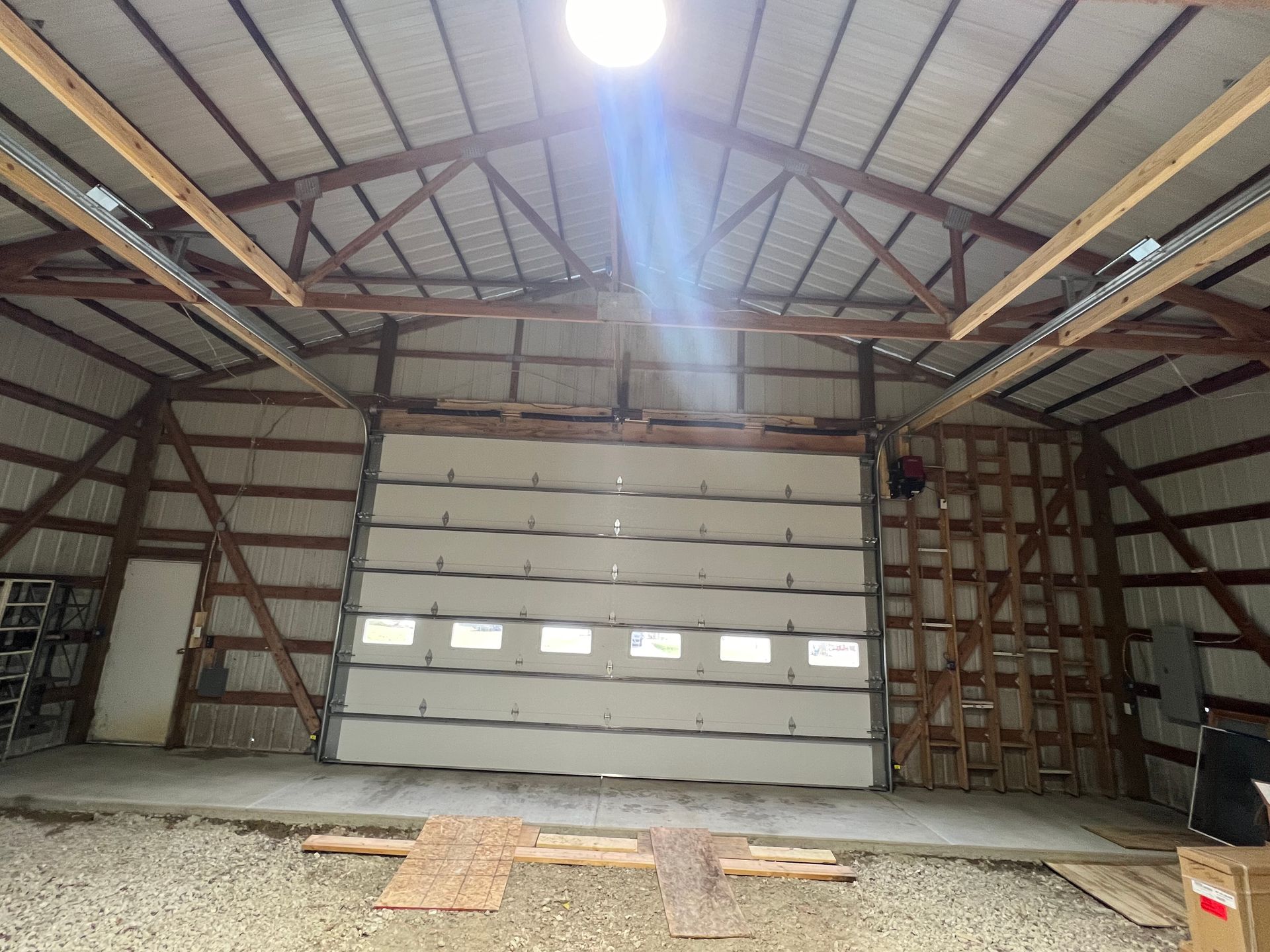 Empty warehouse interior with a large white garage door and exposed wooden roof beams
