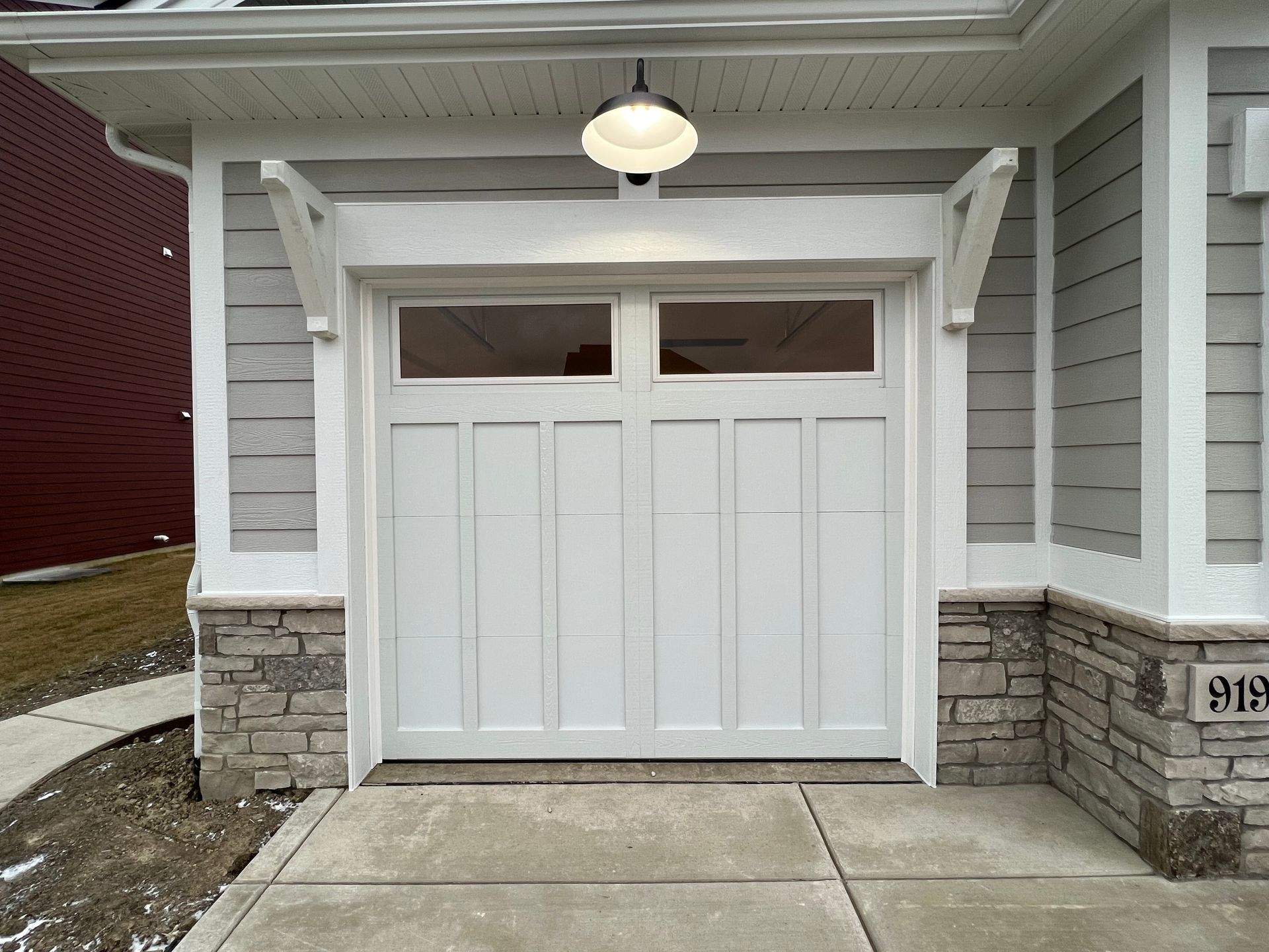 White garage door under a porch, with stone pillars and a hanging light fixture.