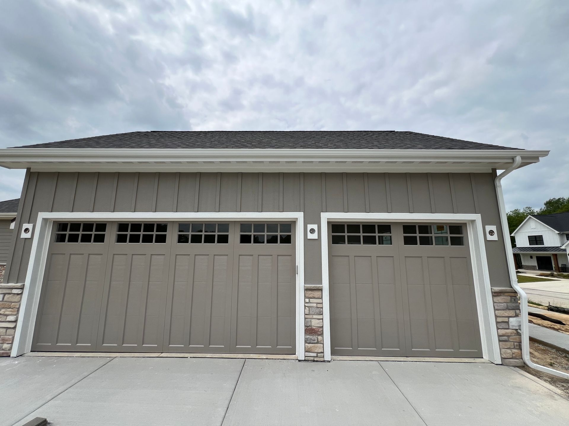 Two-car gray garage with white trim and a driveway under a cloudy sky