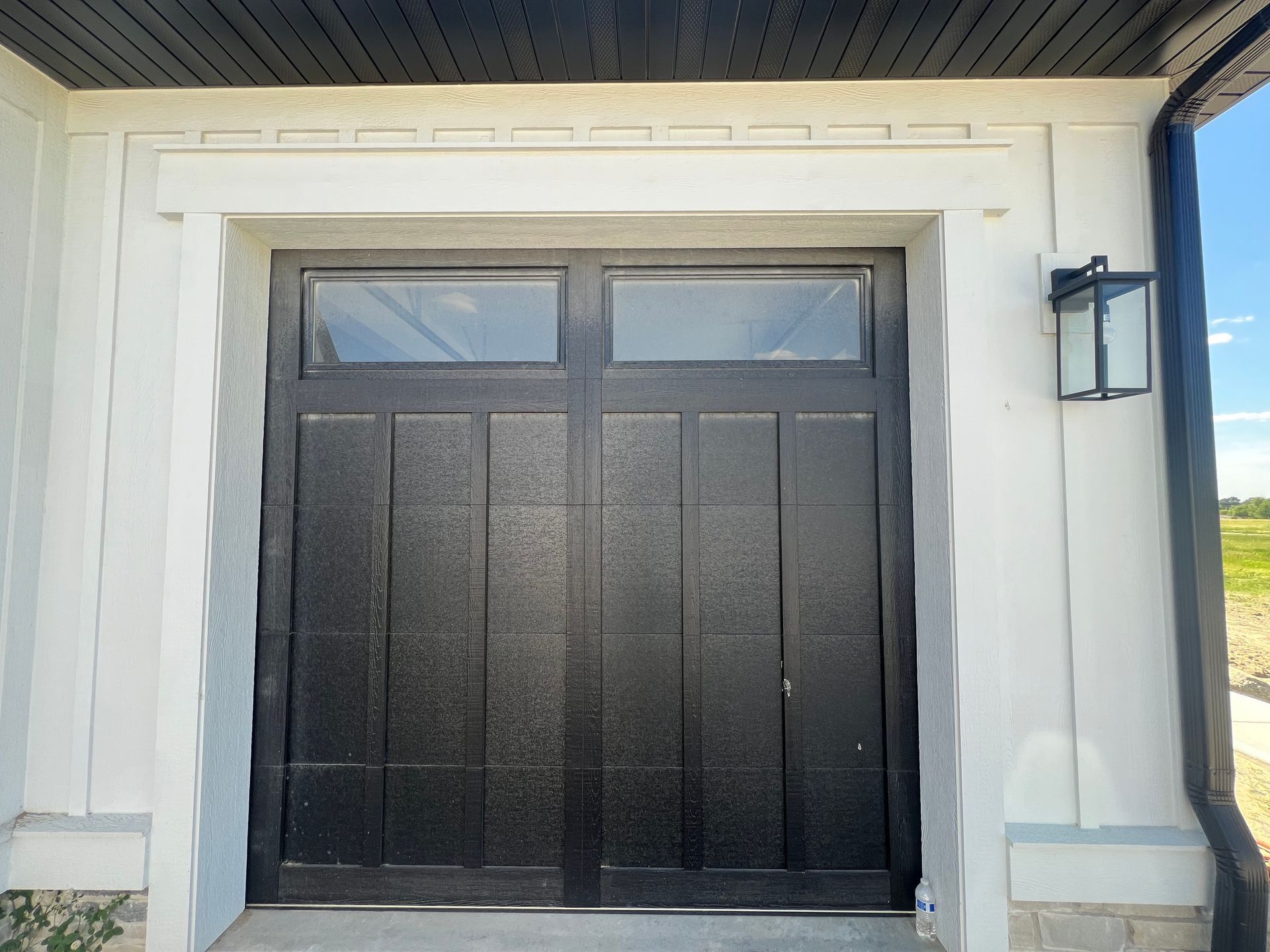 Black double front doors with small transom windows, set in a white exterior wall and trim.