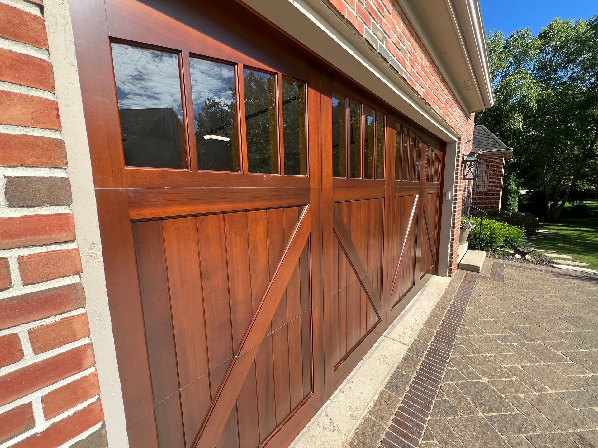 Wooden garage doors with glass panes beside a brick house and paved driveway