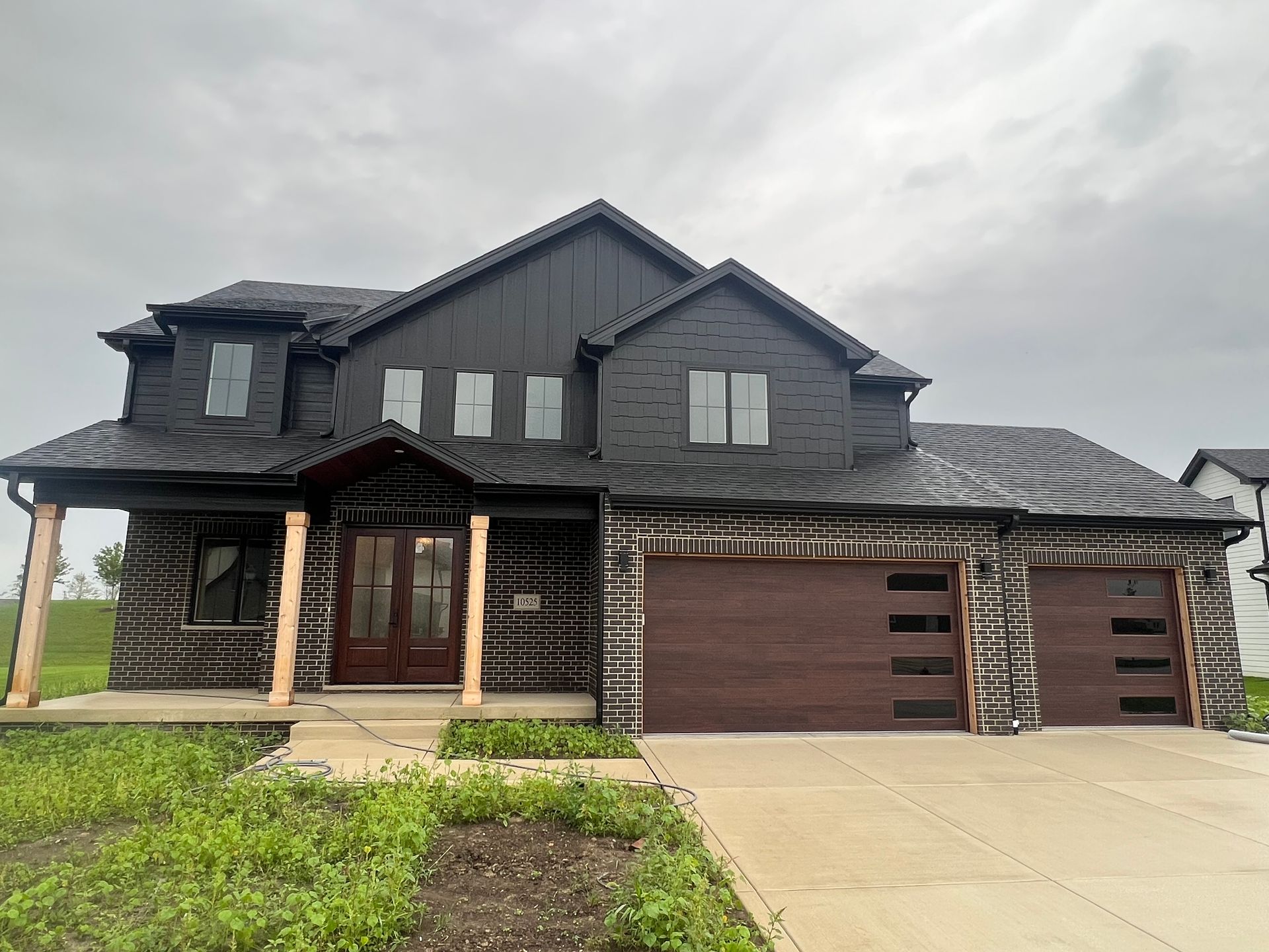 Large dark-gray two-story house with a covered porch, double garage, and concrete driveway under cloudy sky