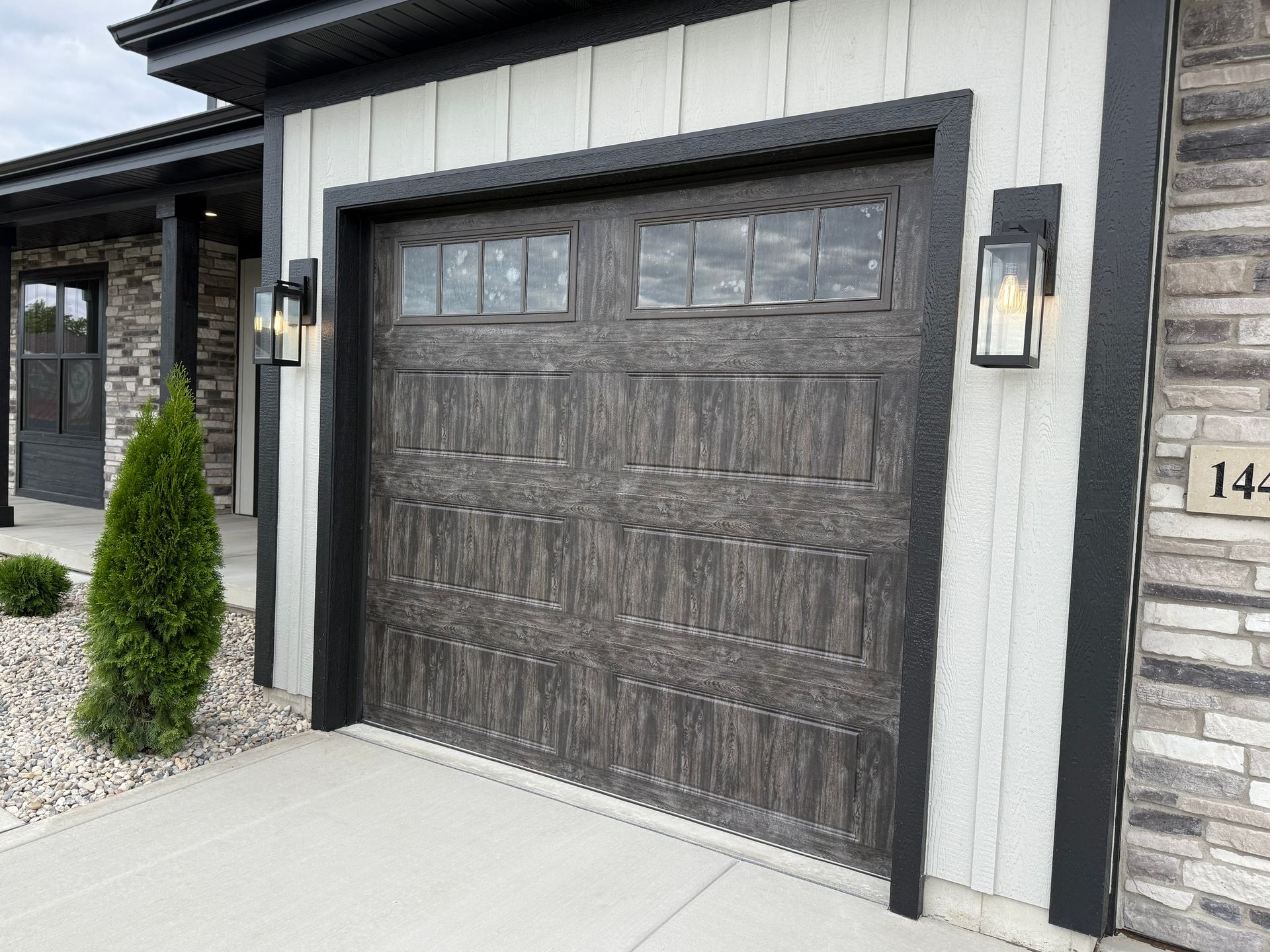 Modern garage door on a house exterior with gray stone trim and a white wall panel