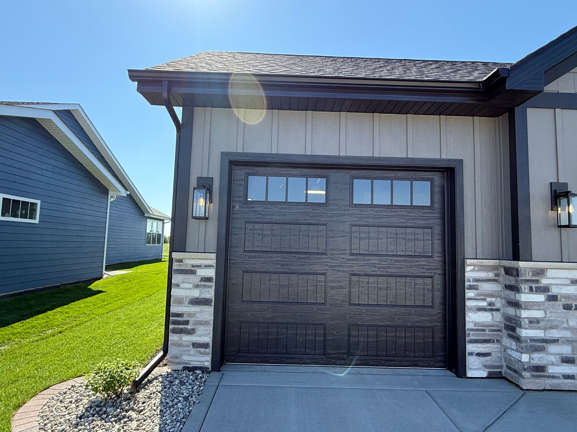 Modern house exterior with a dark garage door, stone siding, and bright sun glare