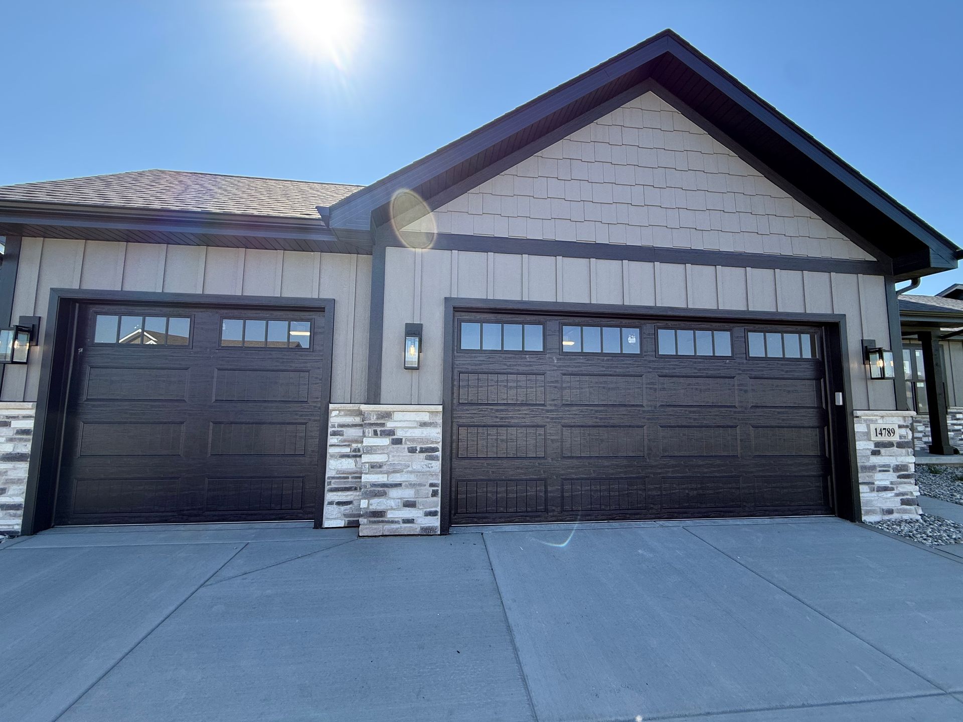 Front view of a single-story house with two dark garage doors and a stone-accent facade in bright sunlight
