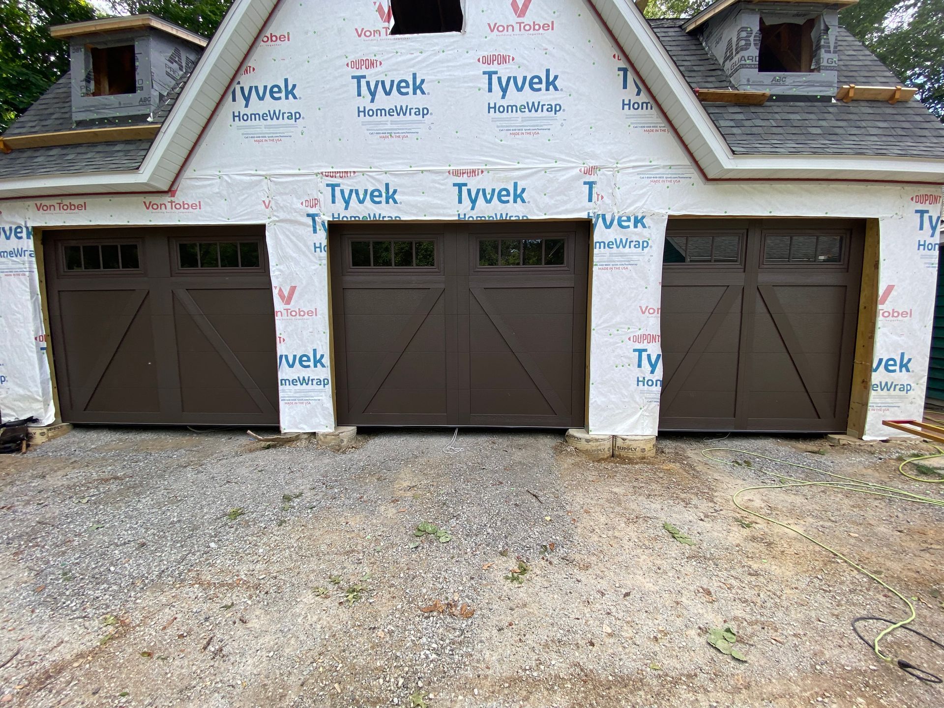 Front of a garage under construction with three brown doors and Tyvek-wrapped walls.