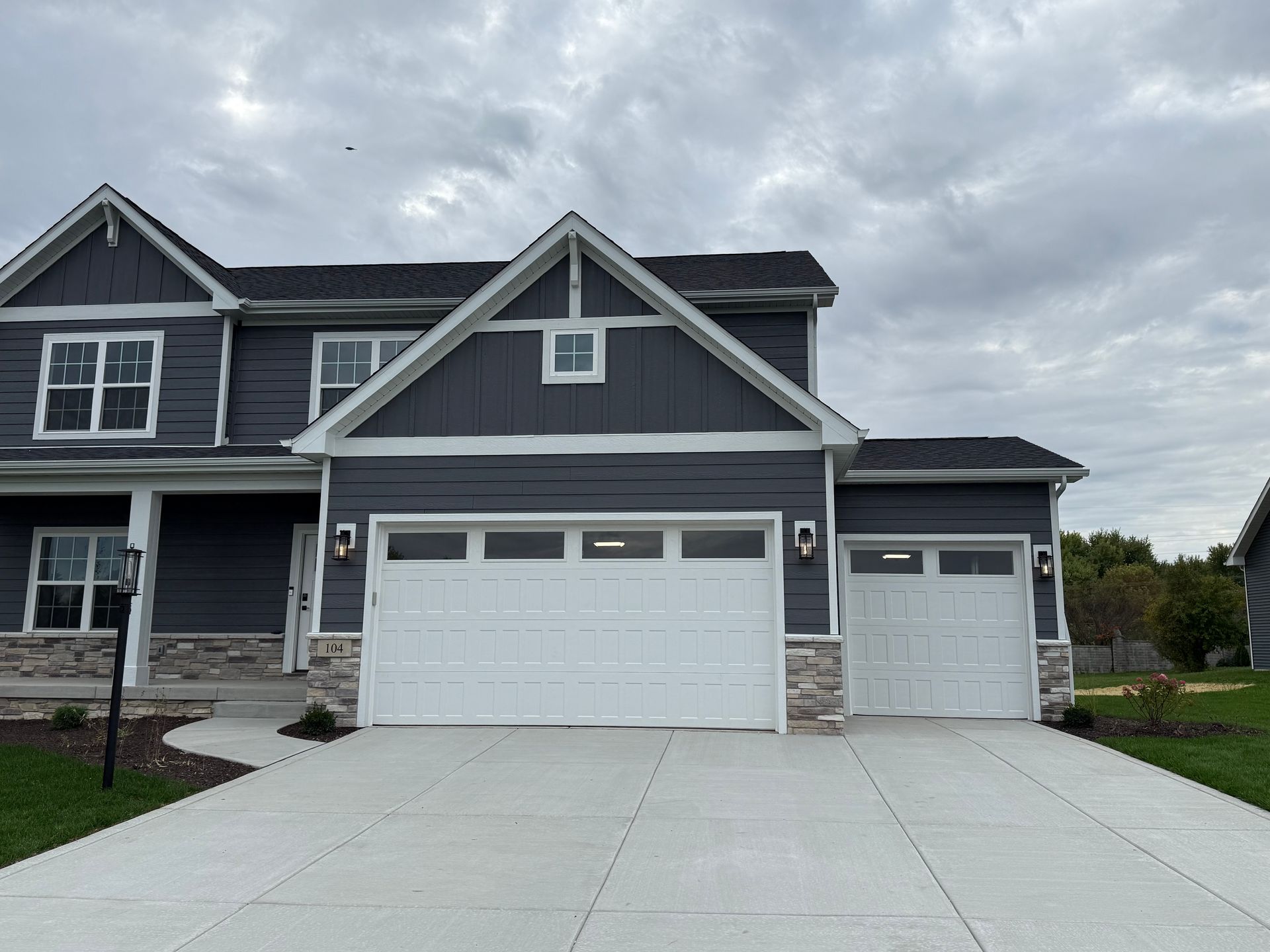 Two-story gray house with white trim, double garage, and a wide concrete driveway under cloudy skies