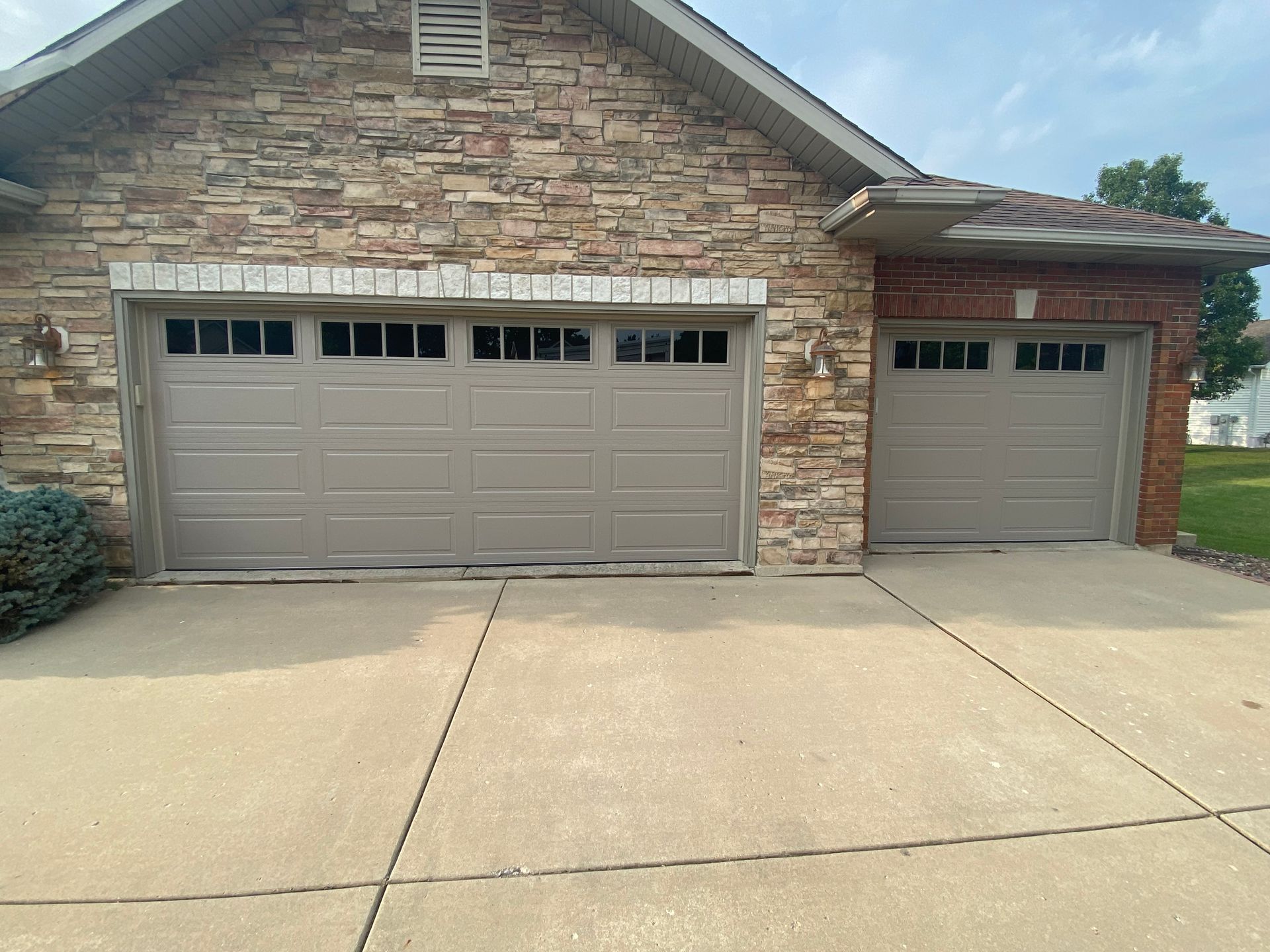 Brick house with two beige garage doors and a concrete driveway under a cloudy sky