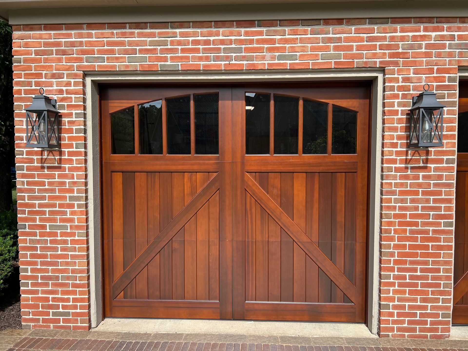 Wooden double garage door set in a red brick wall, with black lanterns on either side.