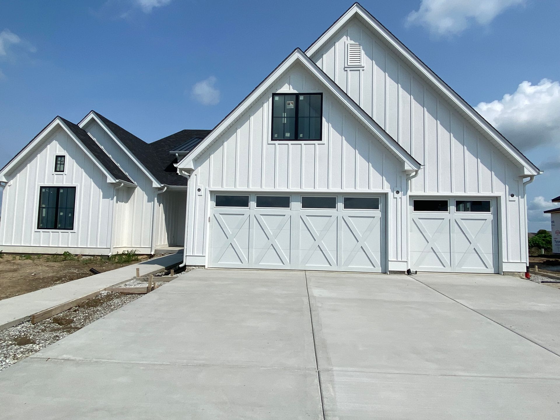 White suburban house with a large two-car garage and wide concrete driveway under a blue sky