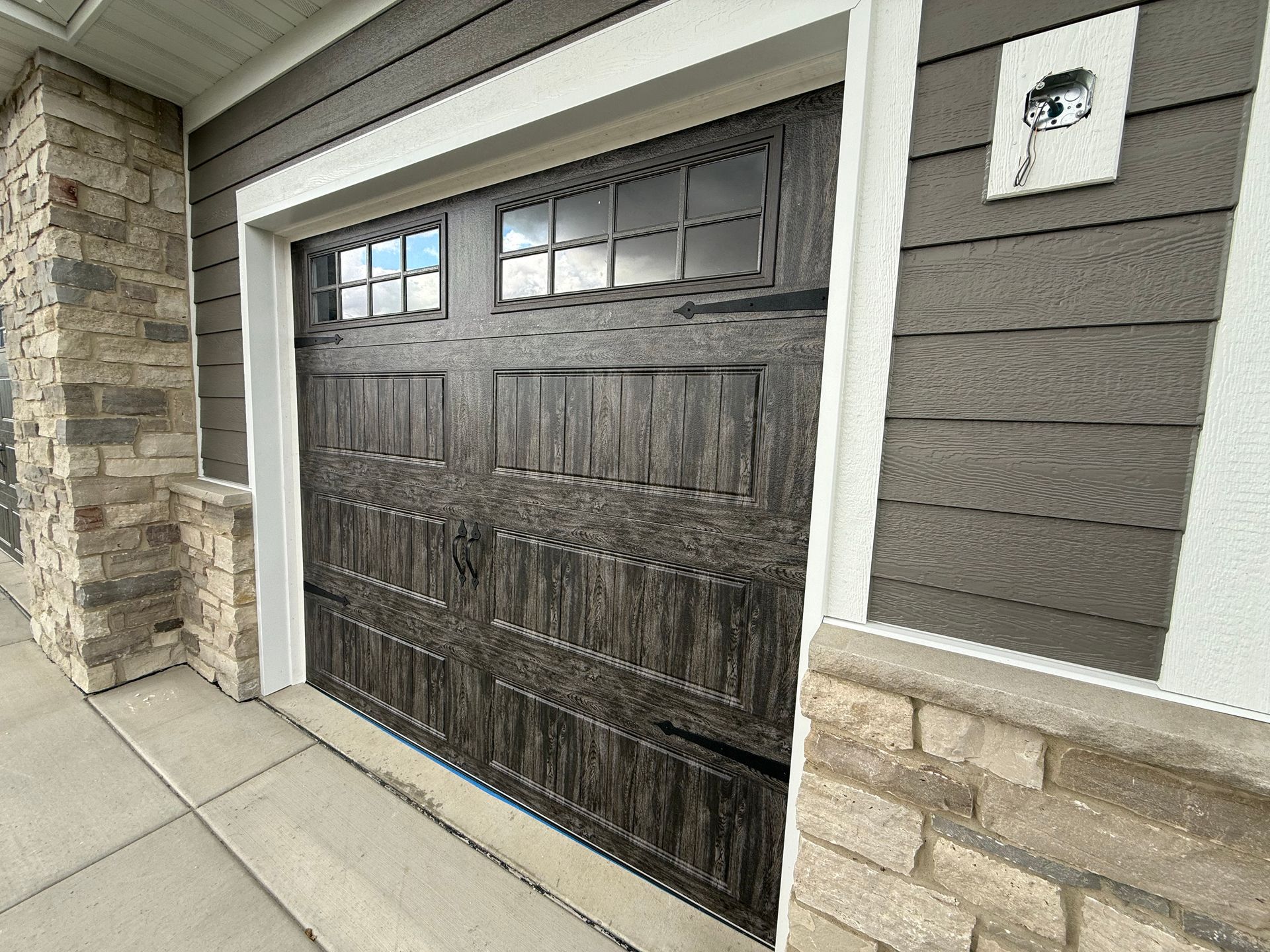 Modern garage door with dark wood panels, stone trim, and gray siding at a house entrance