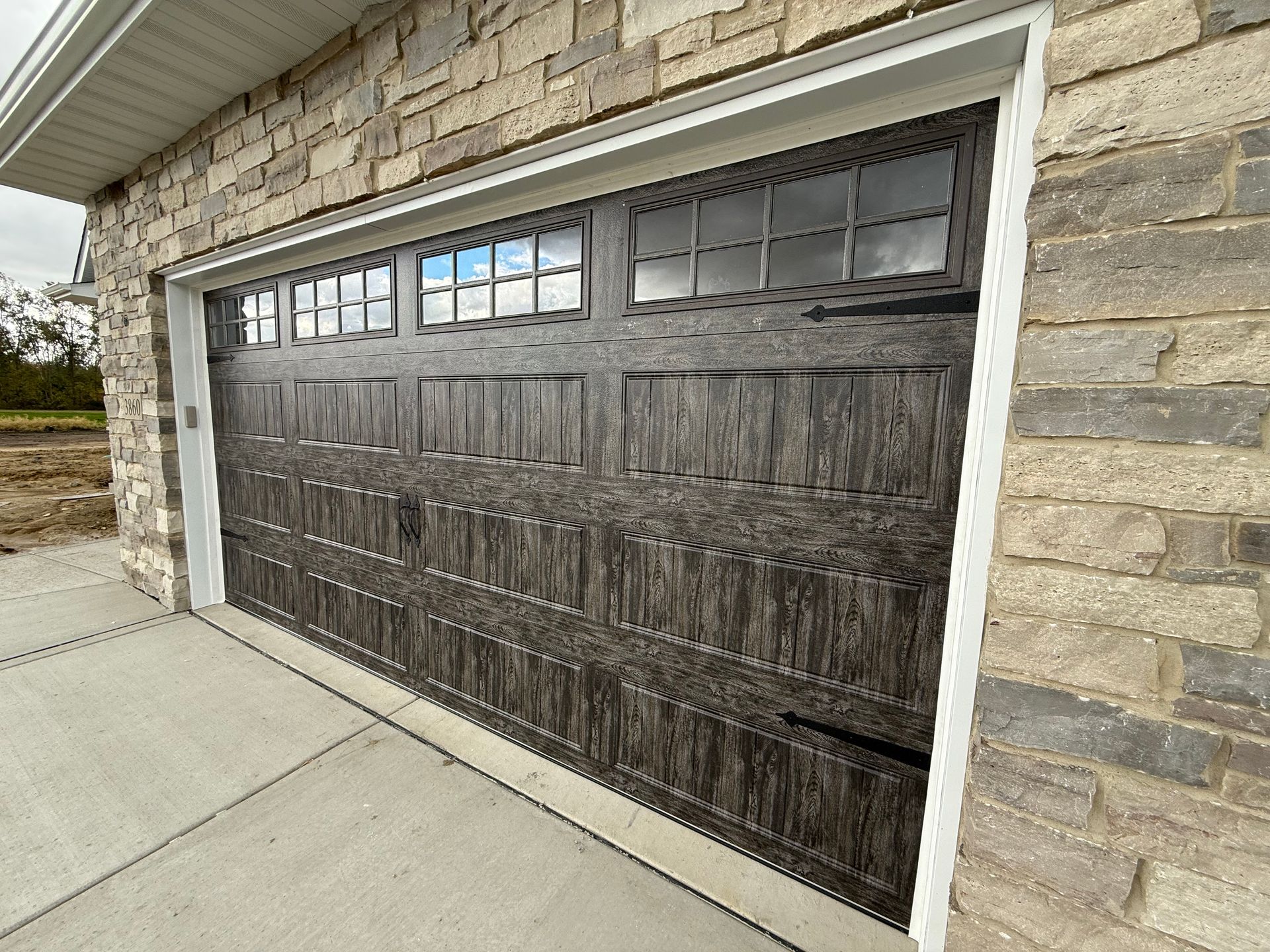 Wooden garage door with small windows, framed by white trim and stone siding