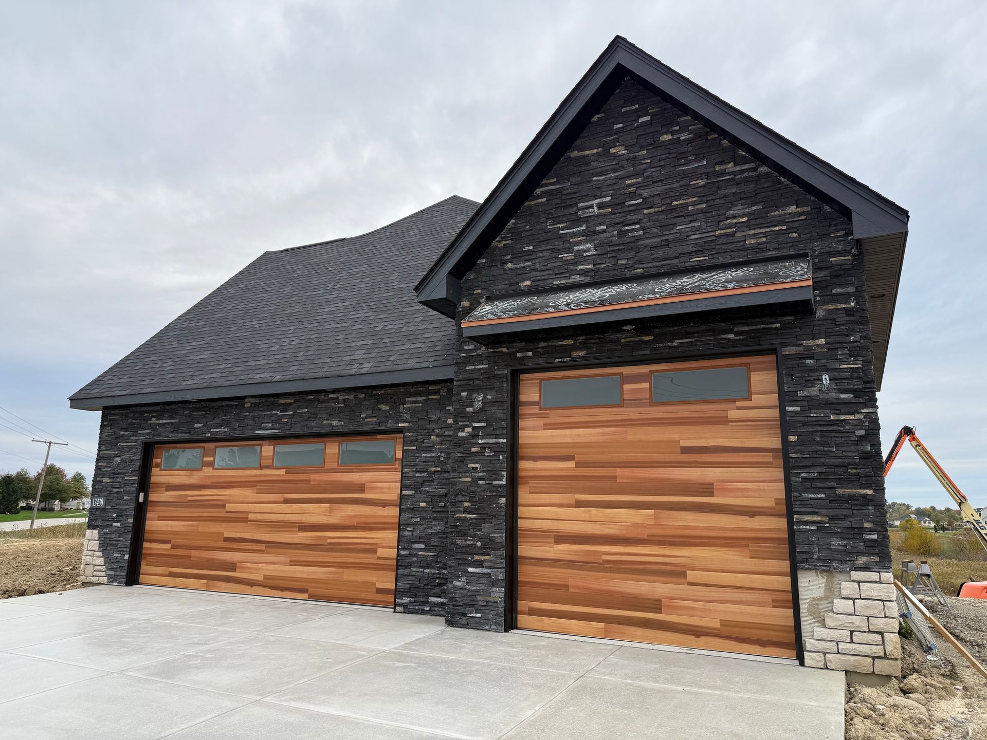 Modern black stone house with two wooden garage doors and a gray shingled roof