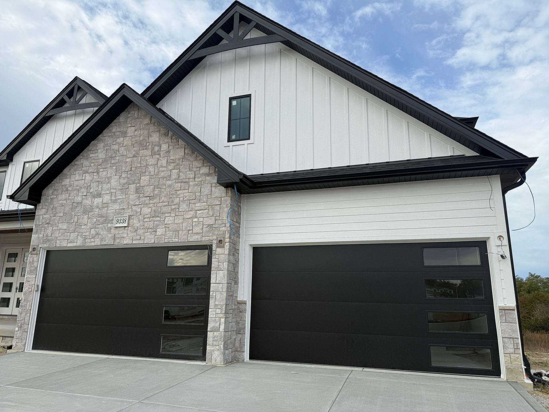 Modern two-car garage with stone and white siding and dark doors under a gabled roof