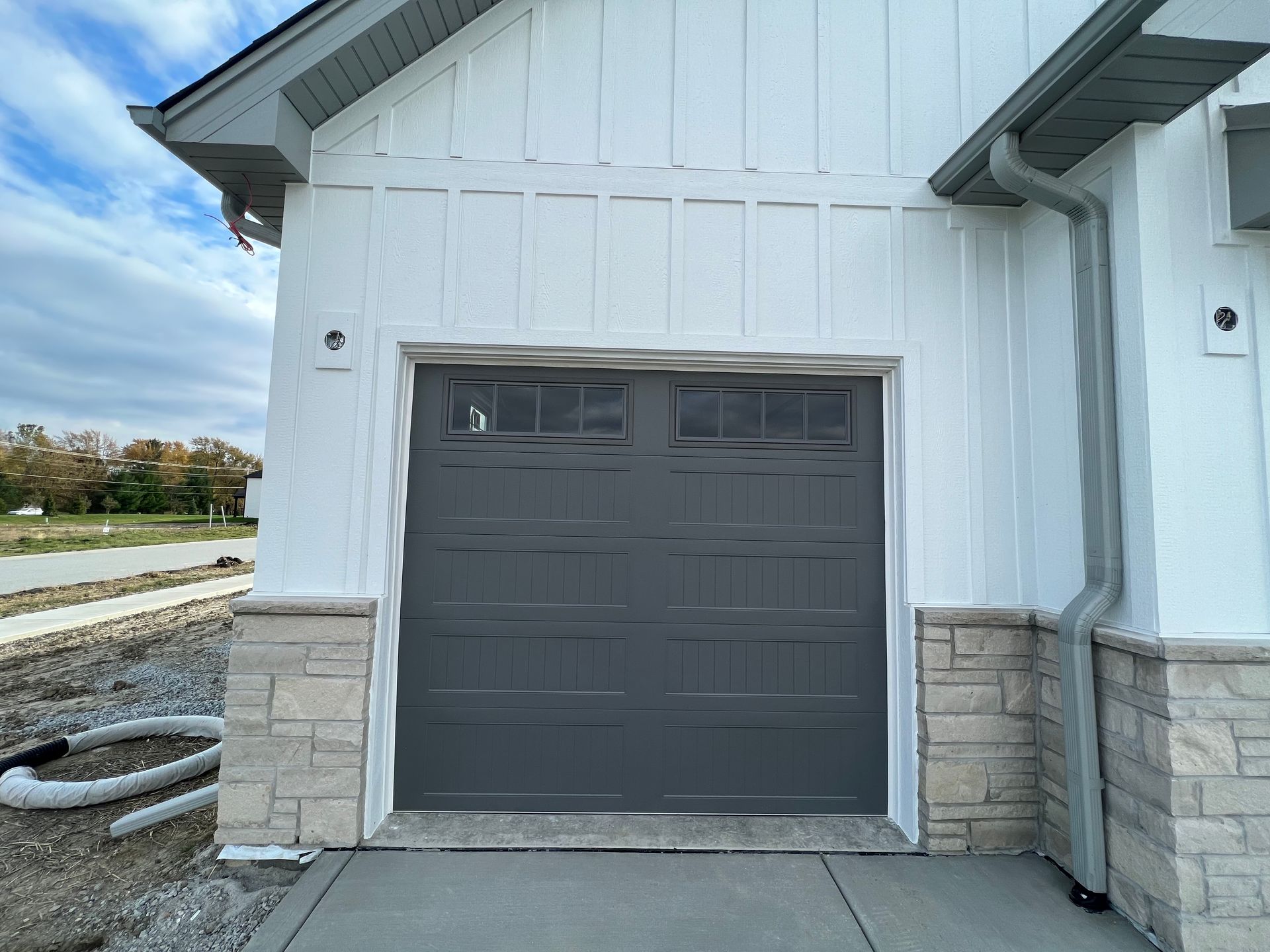 Gray garage door on a white house with stone accents and a gravel driveway