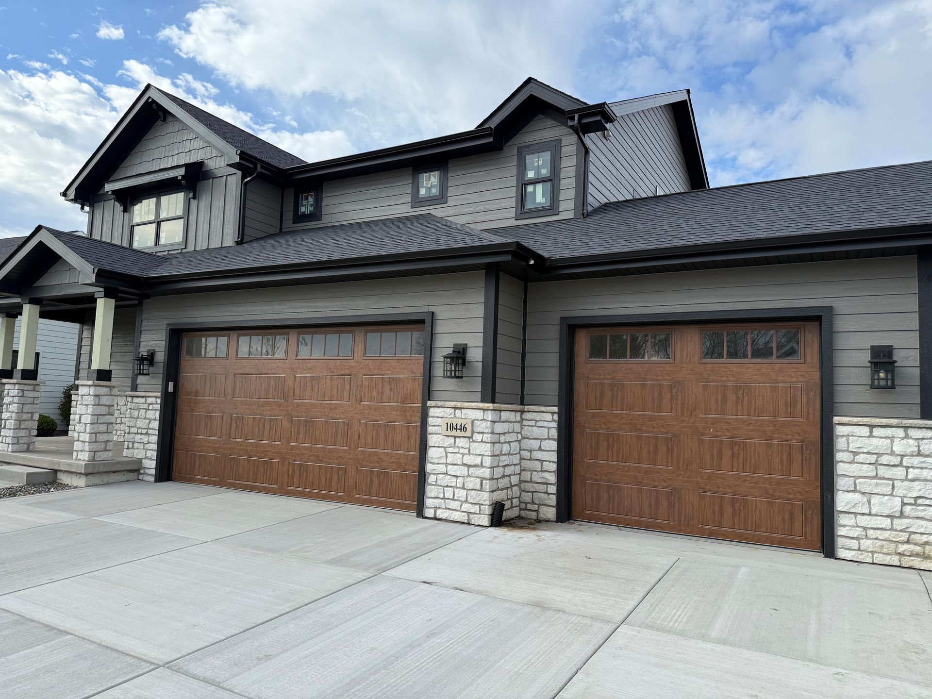 Modern suburban house exterior with stone facade, two brown garage doors, and a concrete driveway