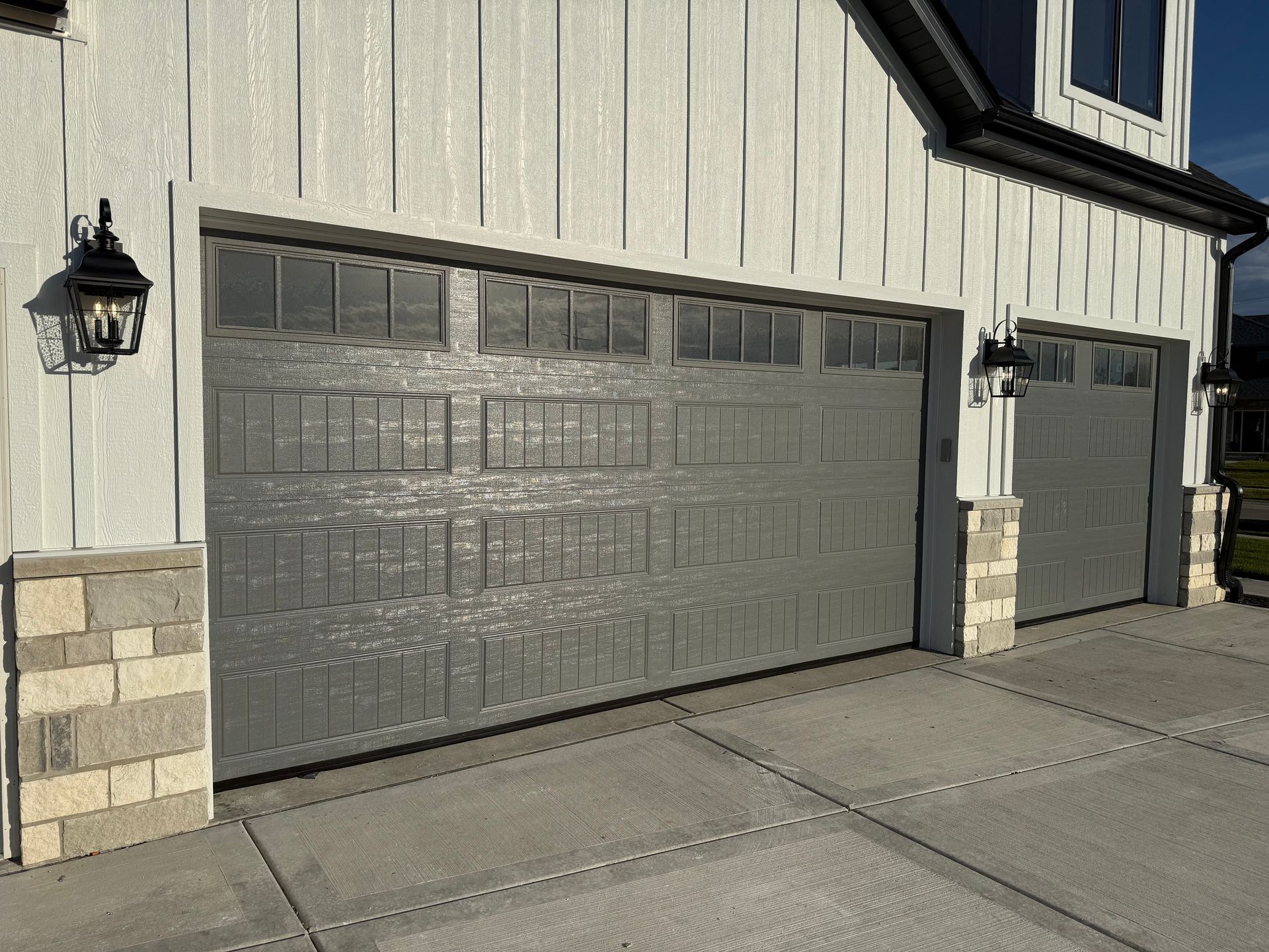 Two gray garage doors on a beige house with stone pillars and a driveway.