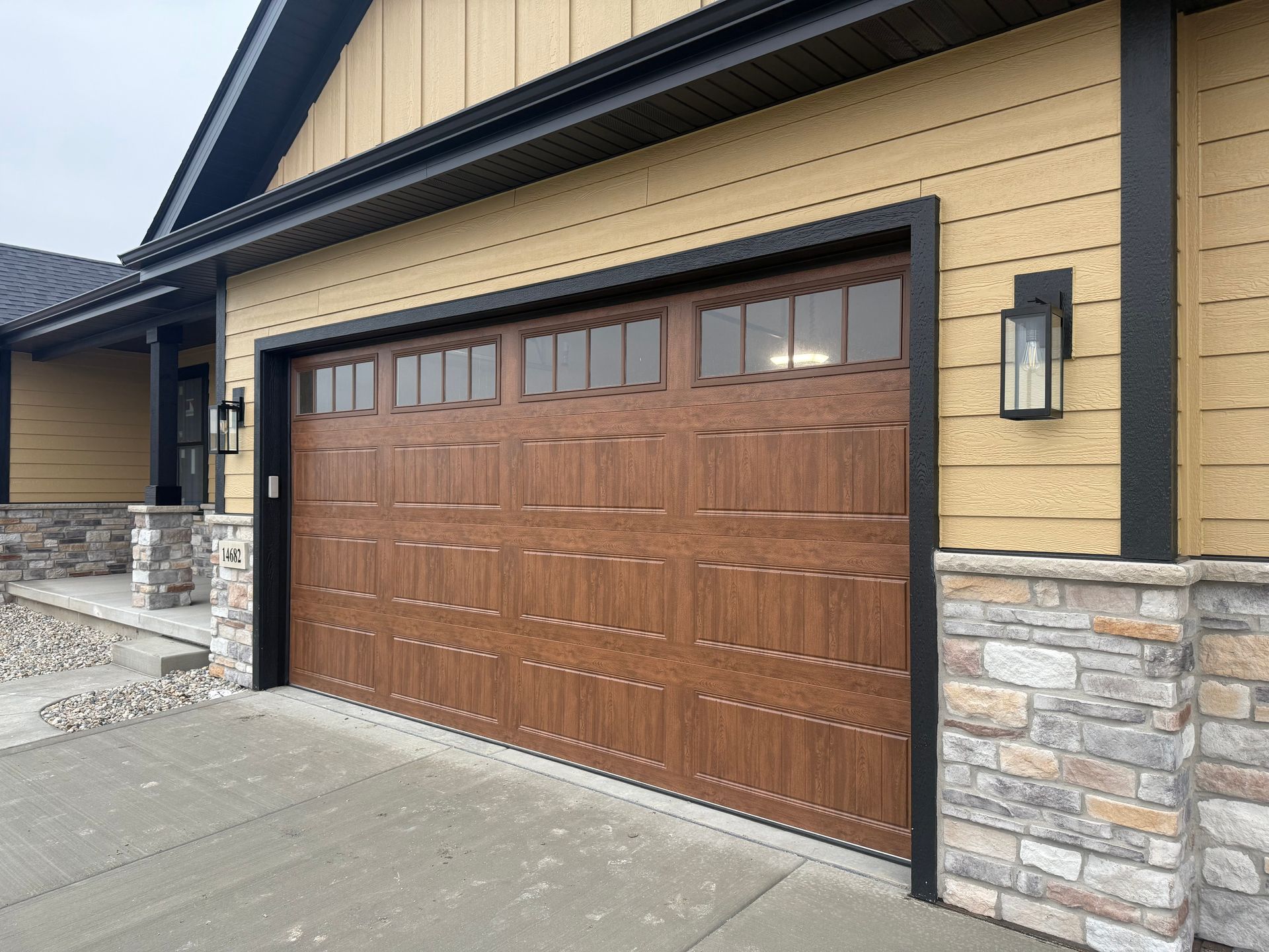 Wooden garage door with windows on a beige house, accented by stone trim and a concrete driveway.
