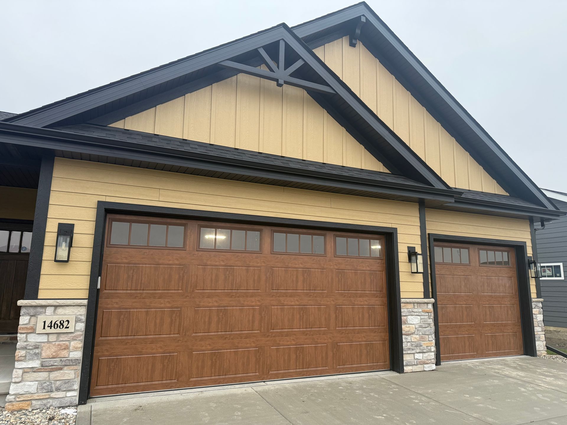Two-car garage with brown doors and beige siding on a stone-accented house exterior.