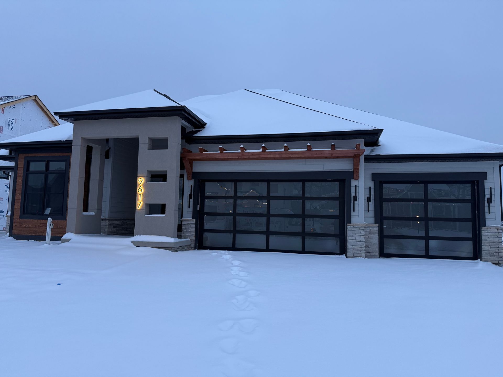 Snow-covered modern house with two garage doors at dusk