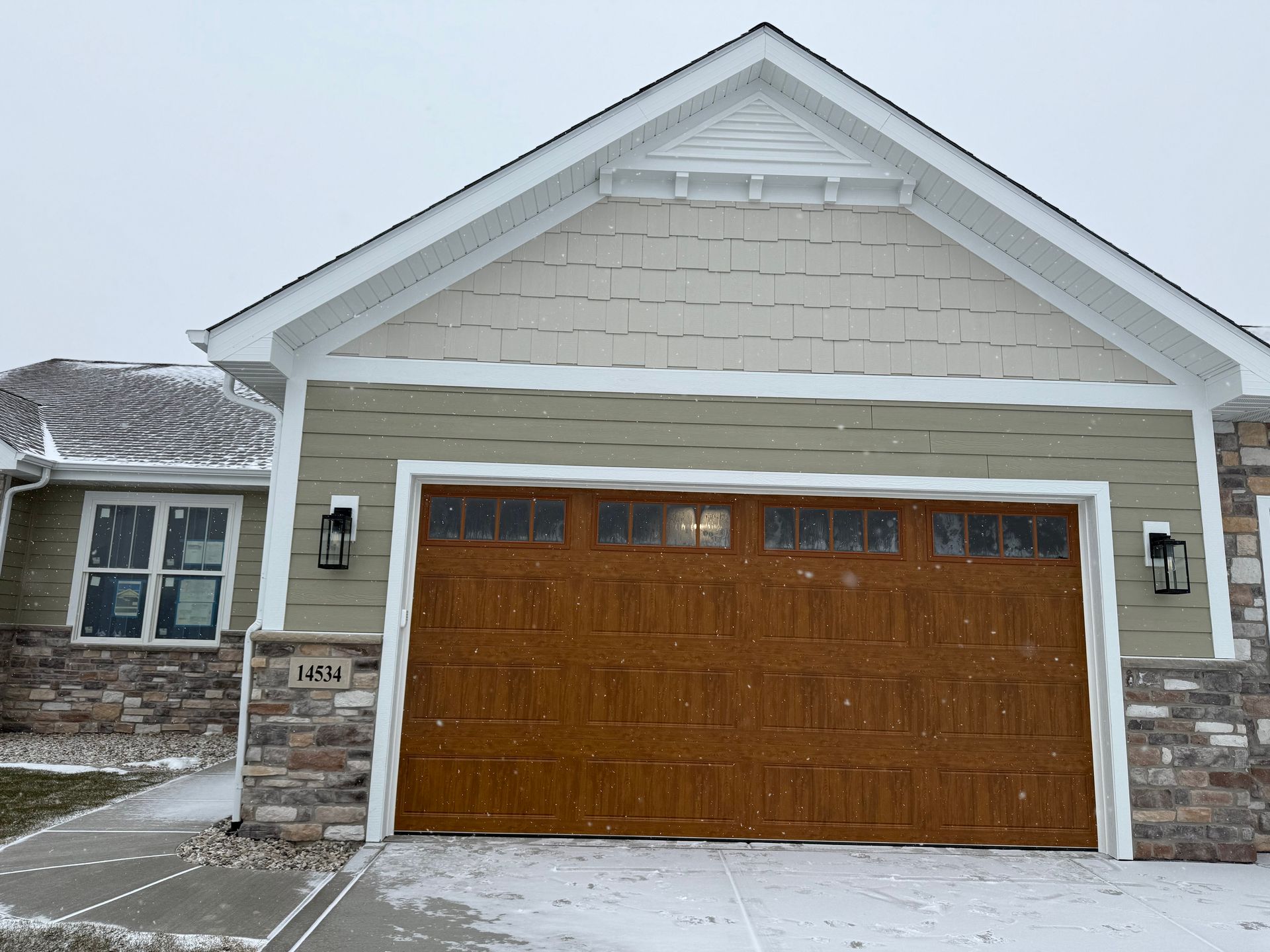 Snowy suburban house with a brown garage door and stone siding