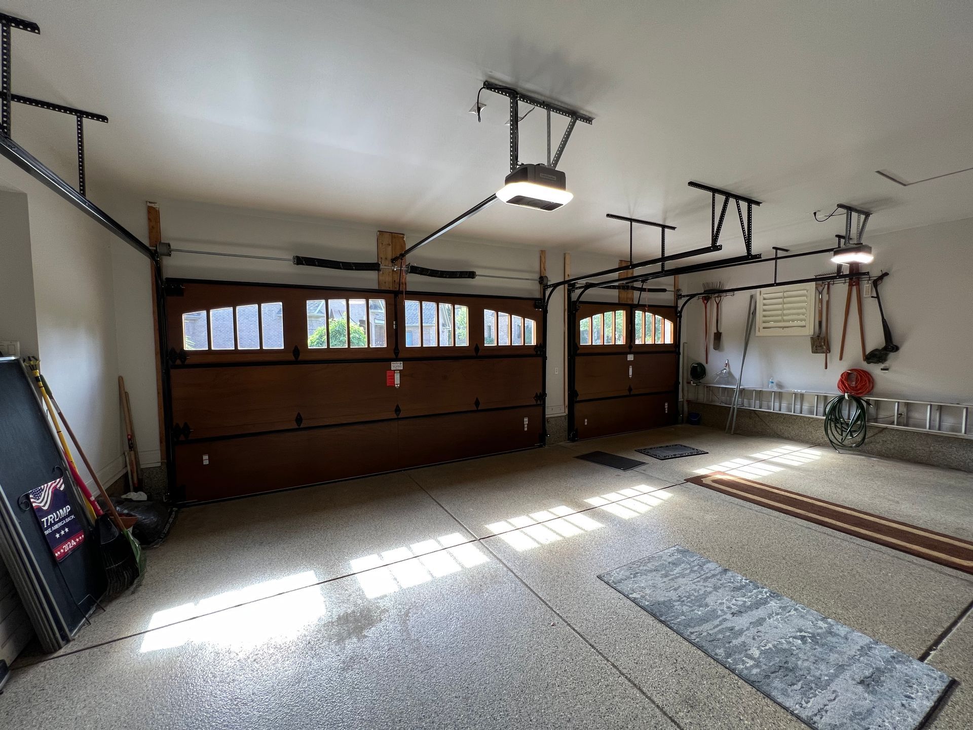 Empty garage interior with open wooden doors, overhead lights, and sunlight on the concrete floor