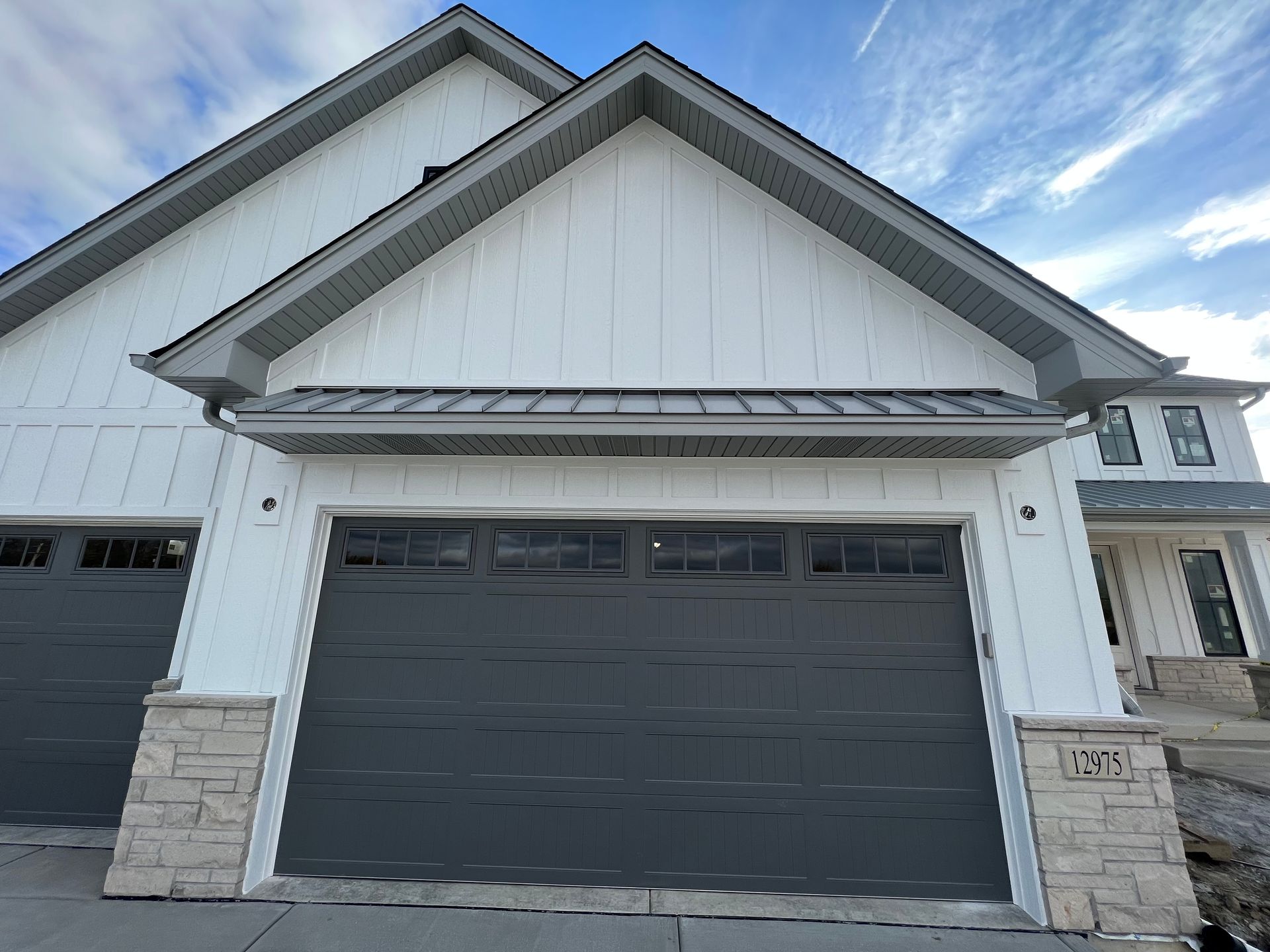 Modern house exterior with dark gray garage door, white siding, and stone accents under a blue sky