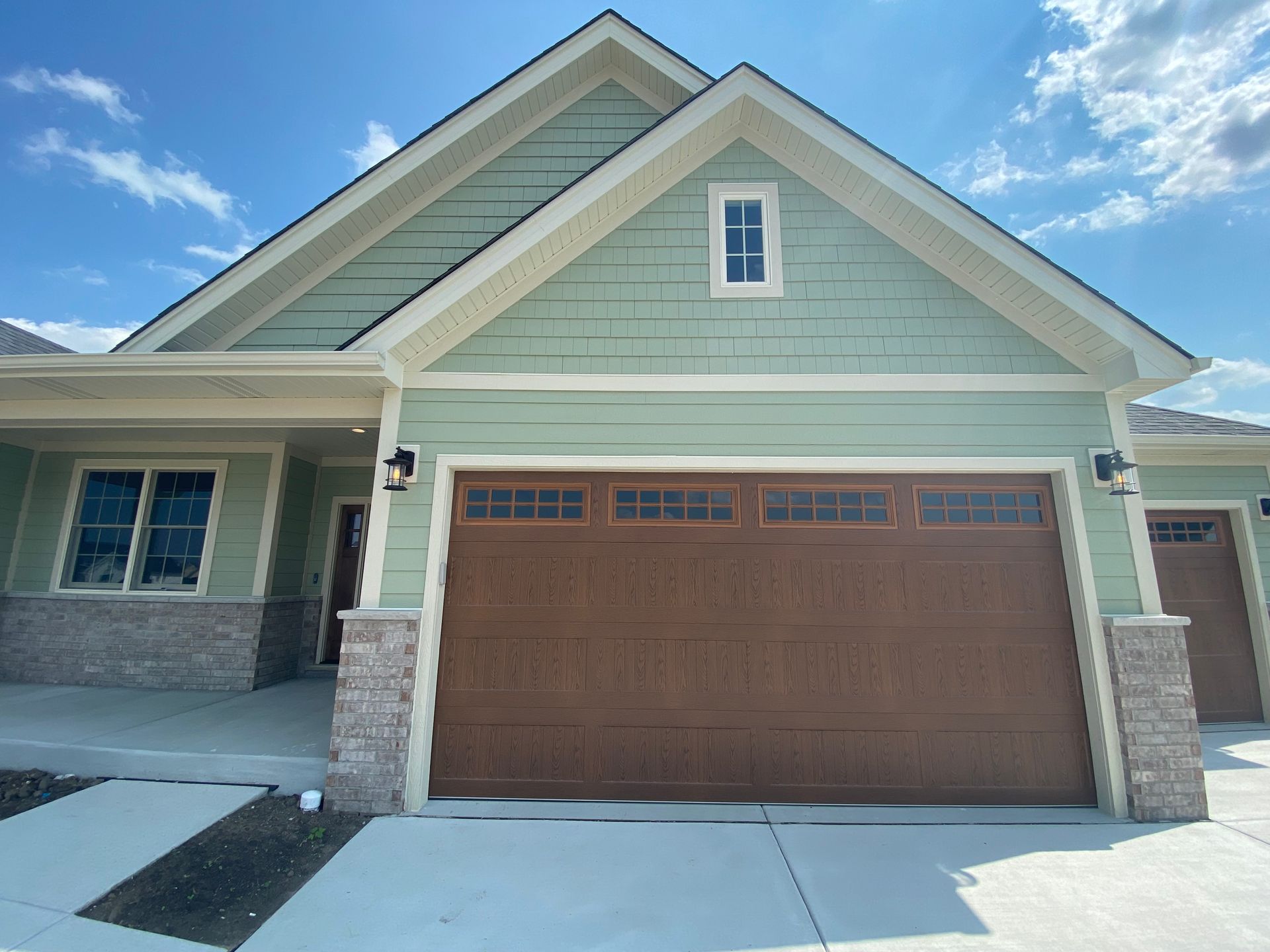 Suburban house exterior with light green siding, brown garage door, and snowy driveway under a blue sky