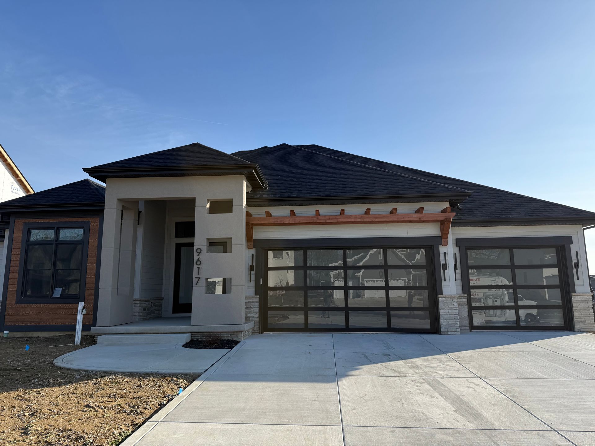 Modern single-story house with a dark roof, front garage, and concrete driveway under a clear blue sky