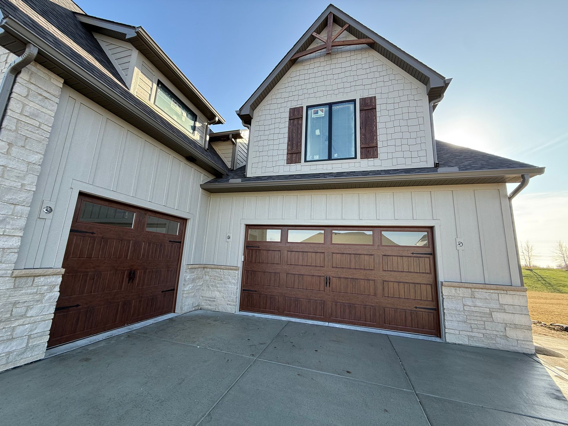 Residential house exterior with white stone walls, brown garage doors, and a driveway under a blue sky