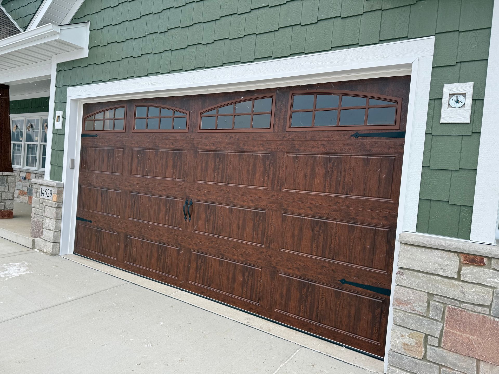 Wooden garage door on a green house exterior with stone accents and concrete driveway