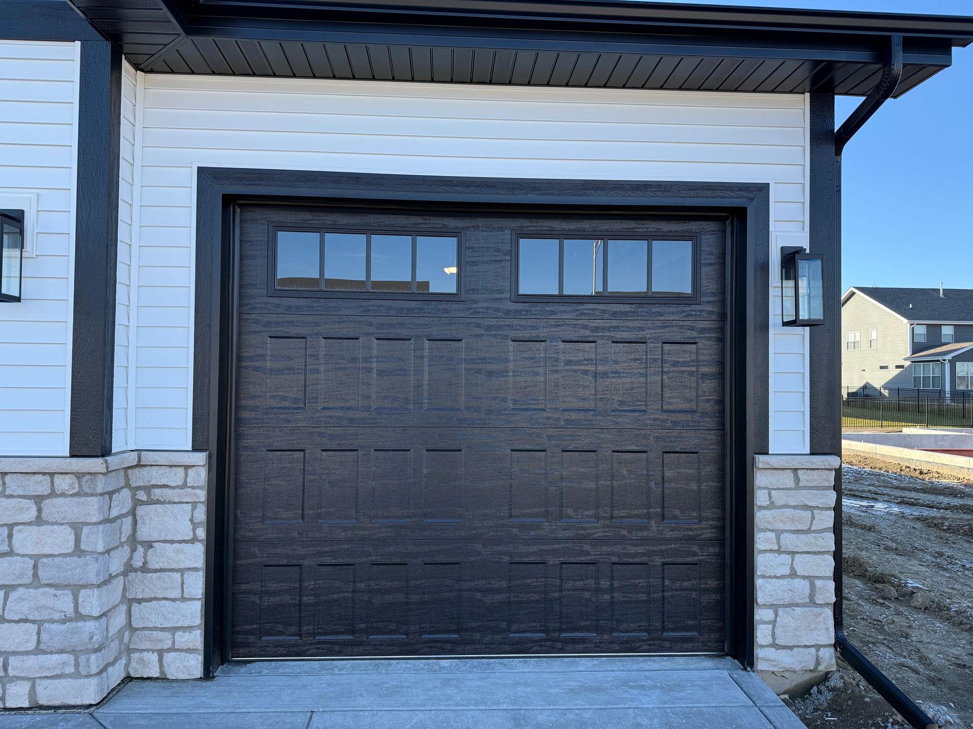 Black garage door with small windows in a white suburban house exterior