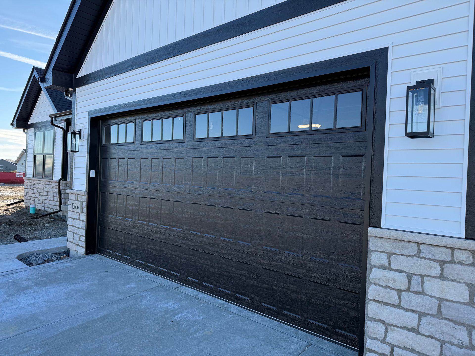 Black garage door on a modern house with white siding and stone trim