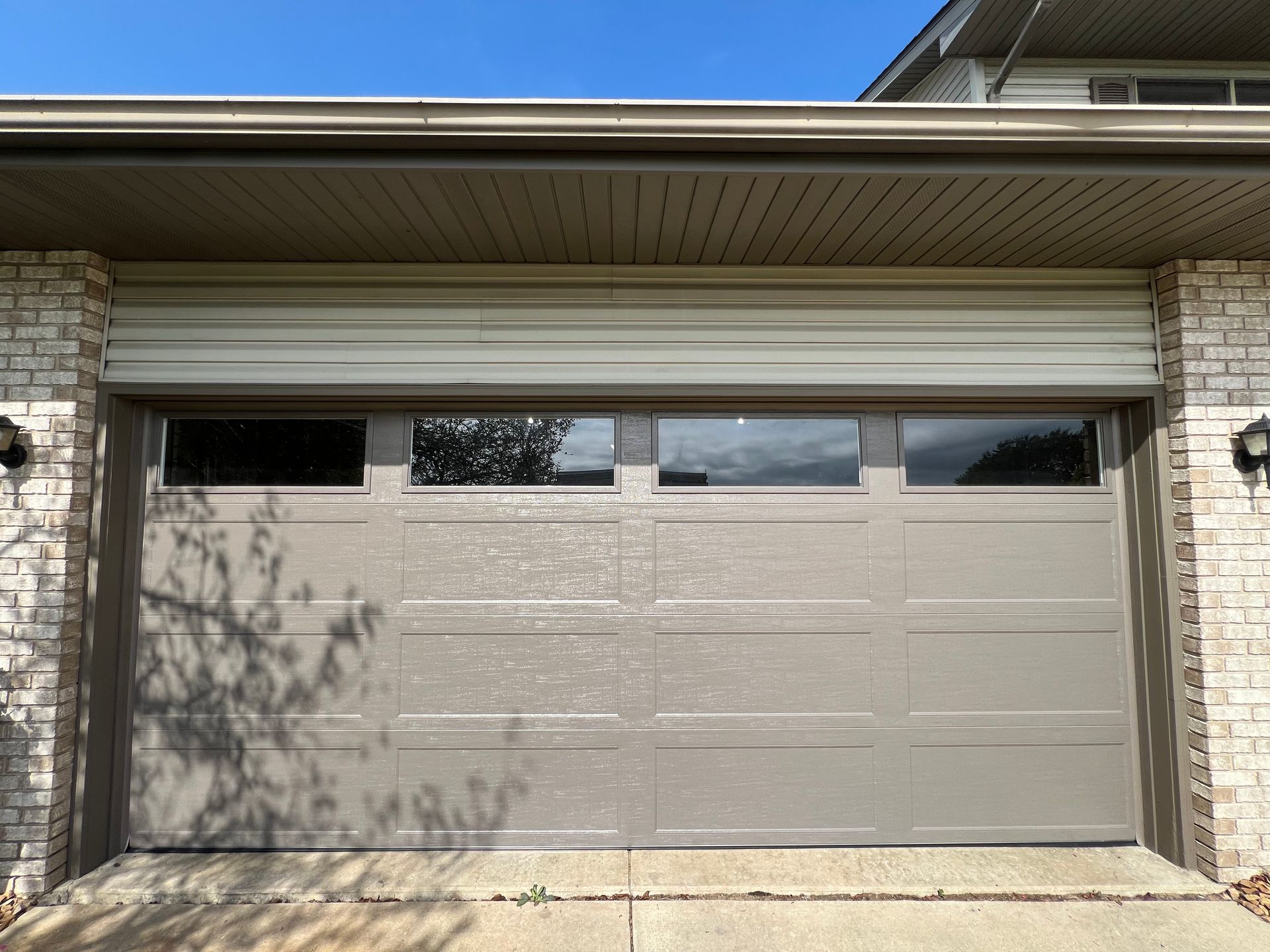 Closed beige garage door on a house with small windows and a brick exterior