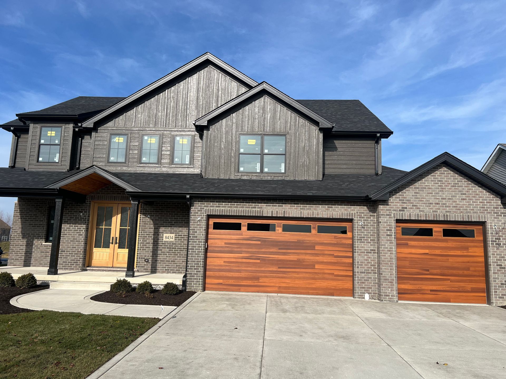 Modern two-story suburban house with stone and wood exterior, double garage, and concrete driveway
