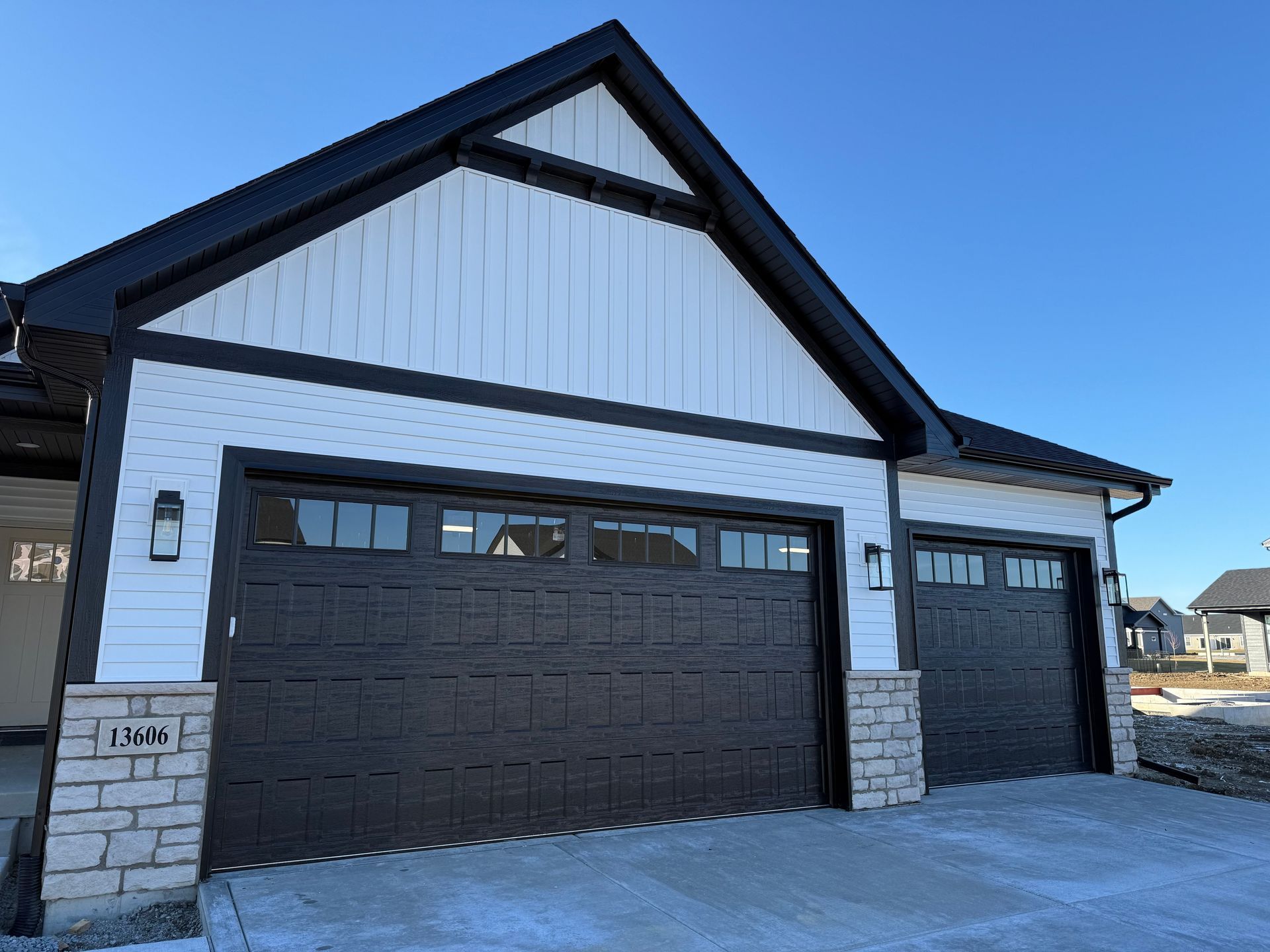 Modern house exterior with two dark garage doors, white siding, and stone accents under a blue sky
