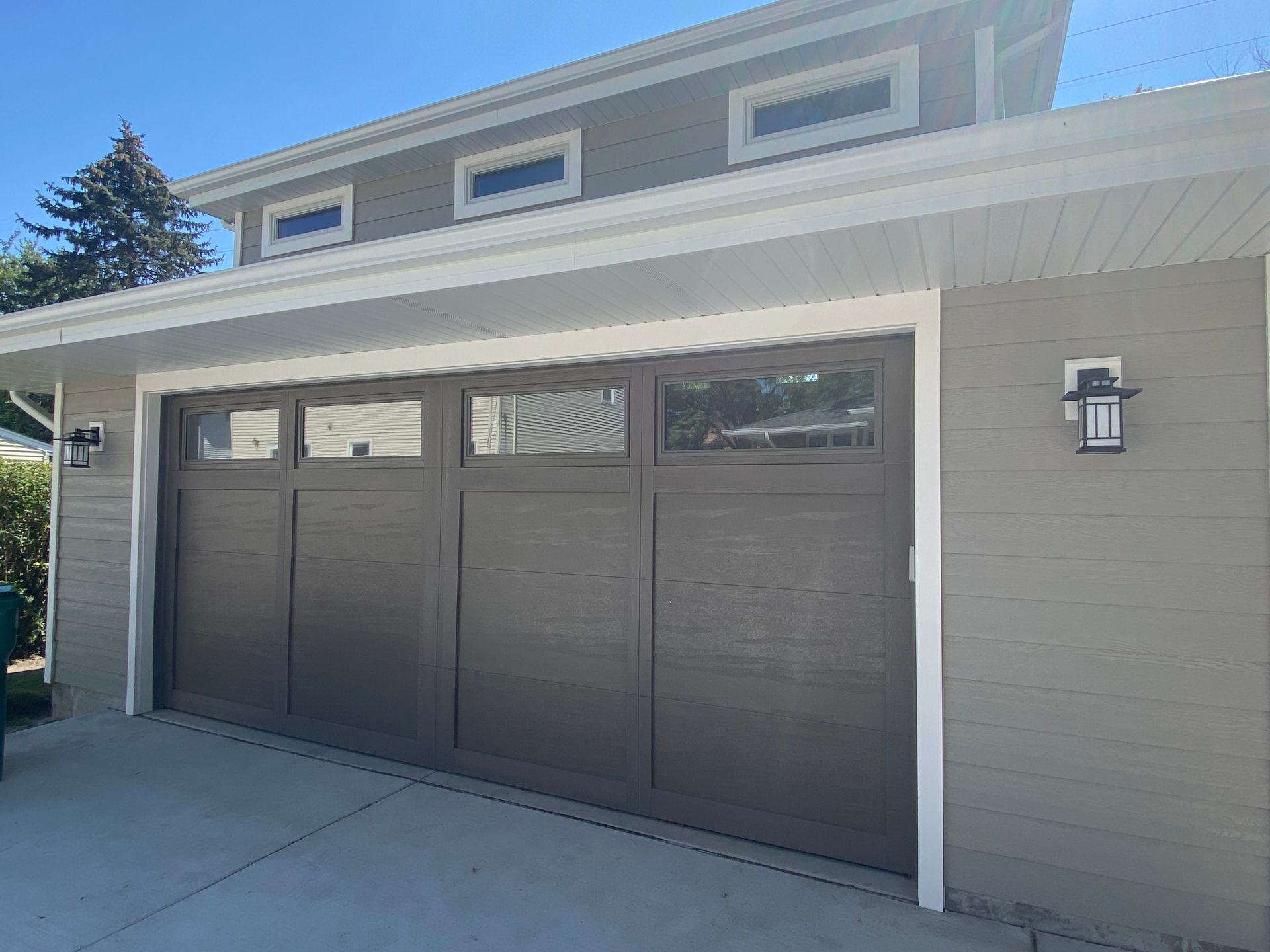 Dark brown double garage door on a beige house exterior with a driveway and wall light