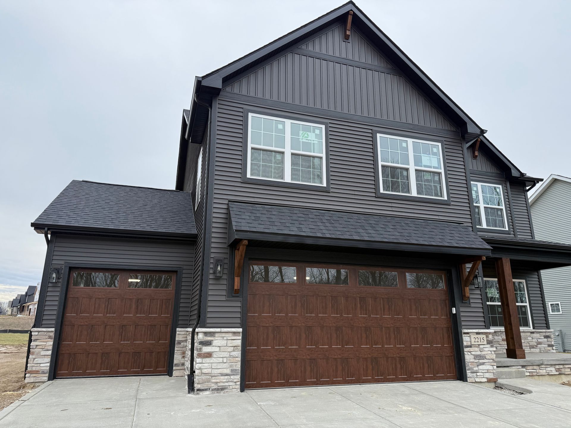 Dark gray two-story house with stone accents and two brown garage doors