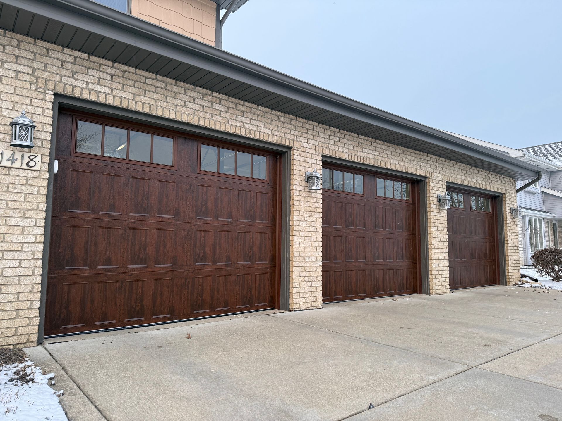 Three dark wooden garage doors on a brick house with a sloped concrete driveway