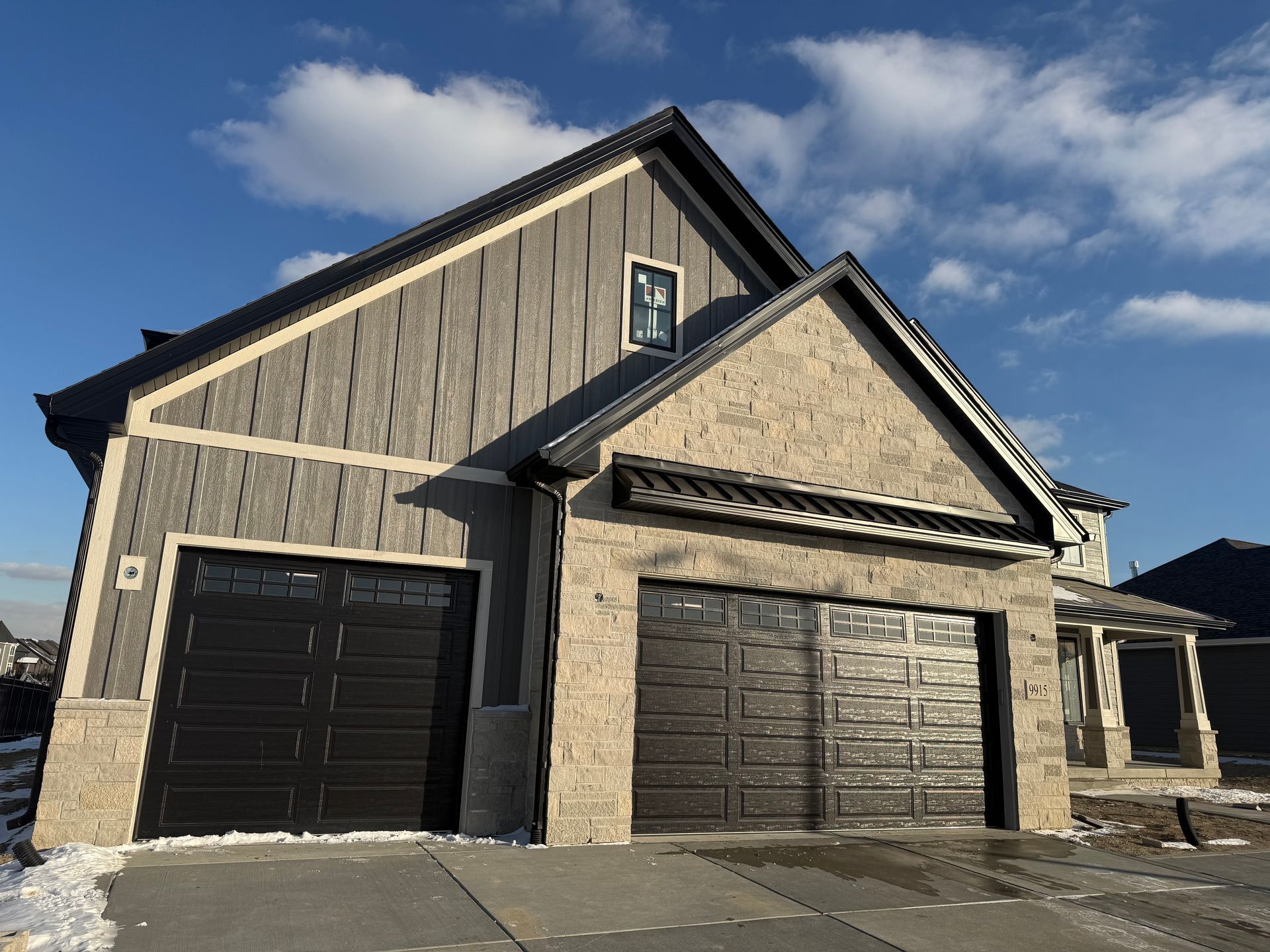 Modern suburban house exterior with gray siding, black garage doors, and blue sky.