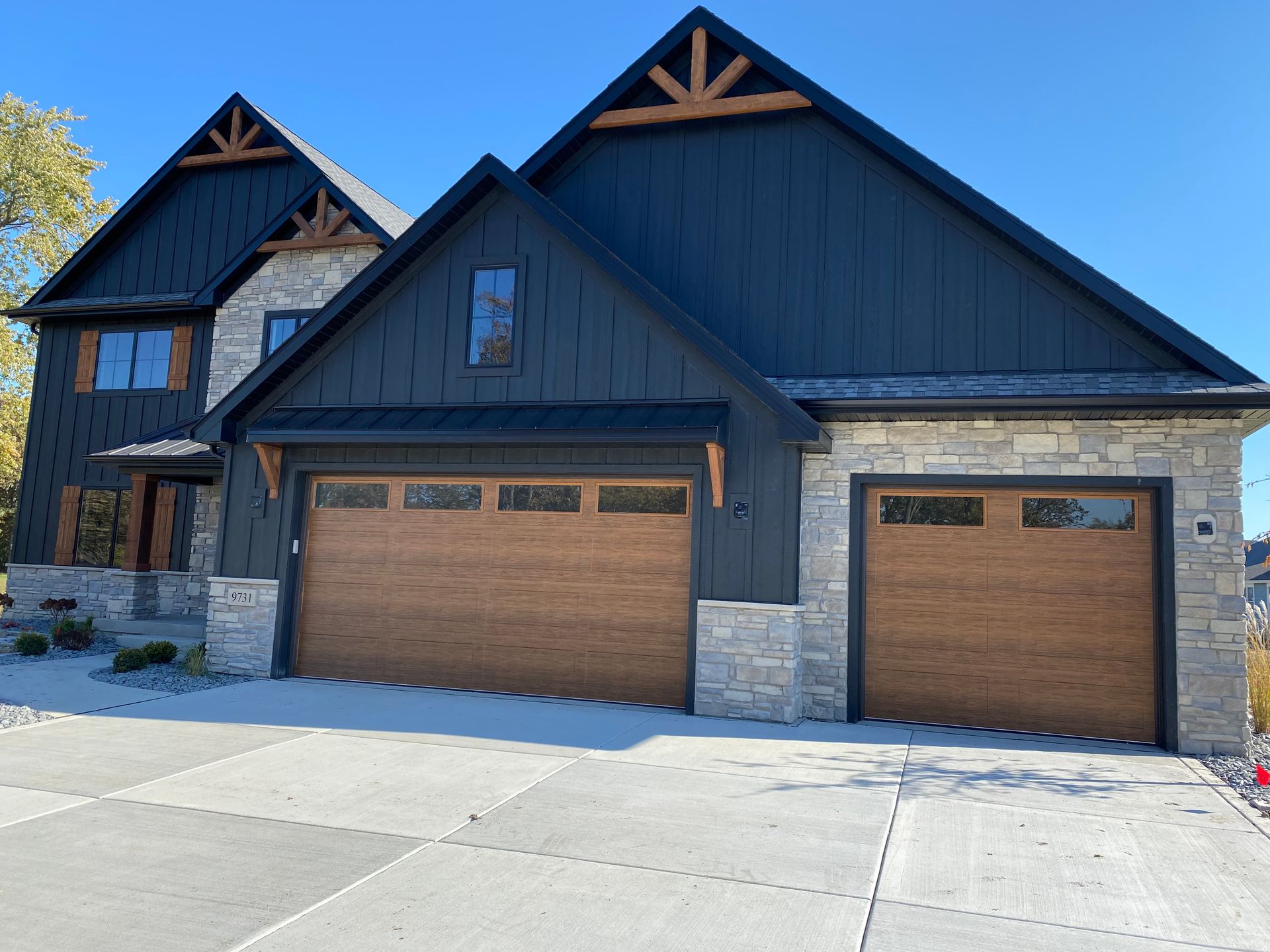 Modern dark blue two-story house with stone accents and two wooden garage doors under a clear sky
