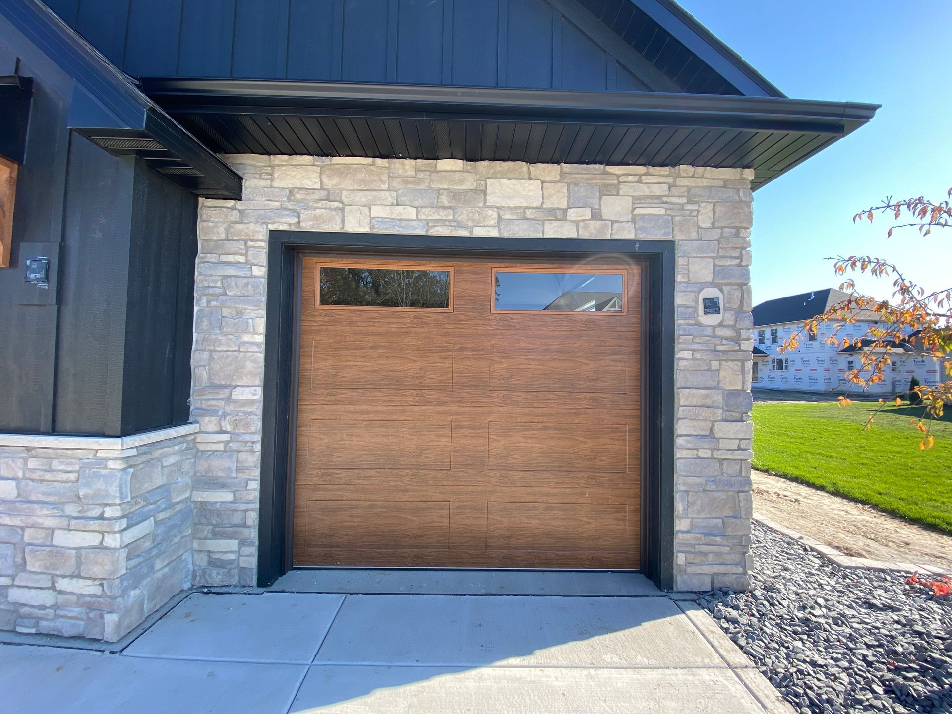 Wood-paneled garage door set in a stone exterior with black trim and a concrete driveway.