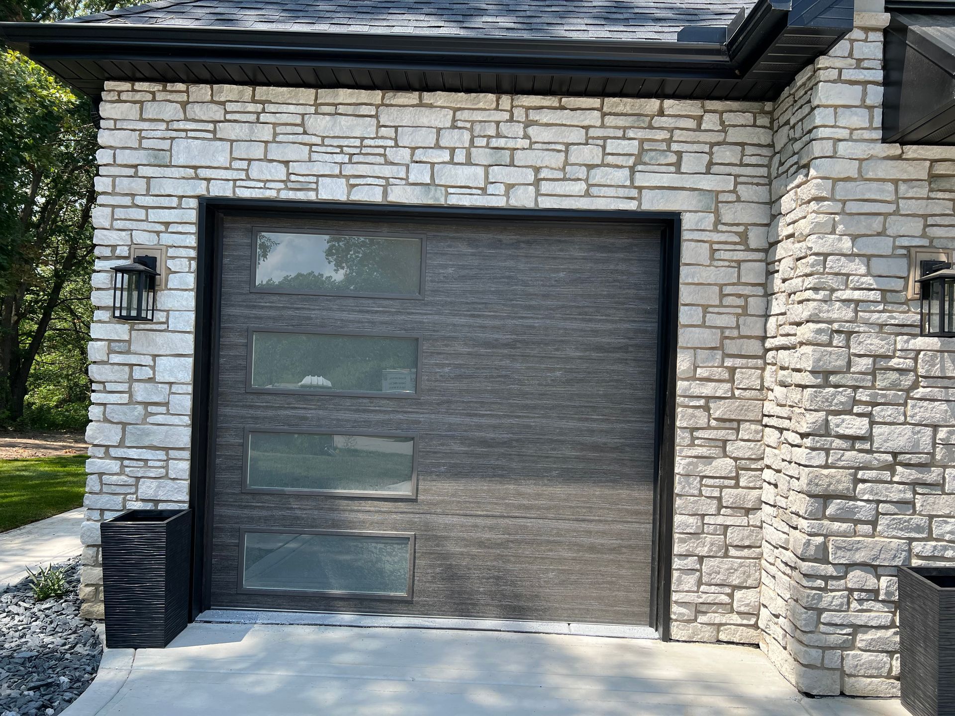 Stone house exterior with a dark gray garage door and wall-mounted lanterns