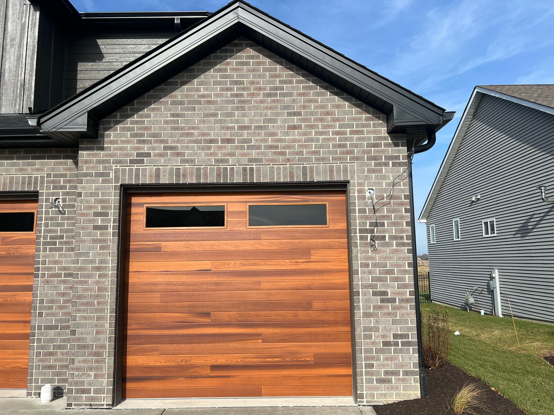 Brick house with a wood-paneled garage door and dark trim under a blue sky